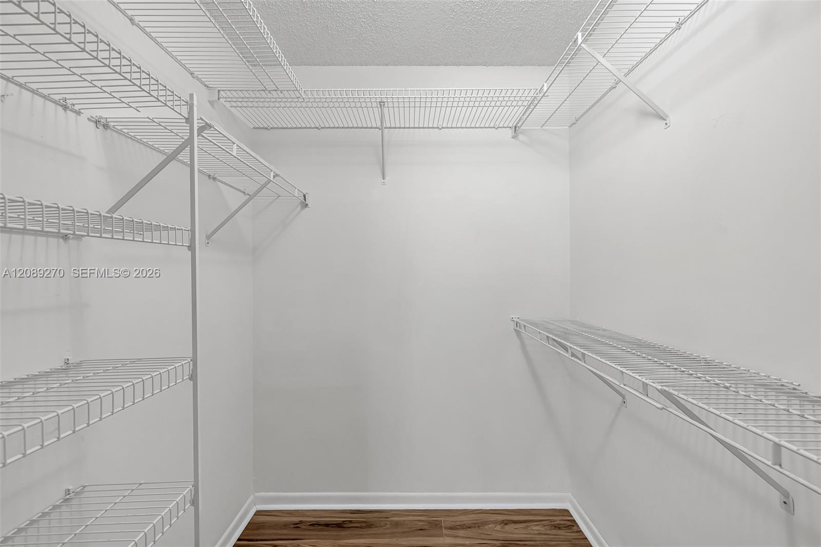 Walk-in closet with extensive white wire shelving and a dark wood-look floor.