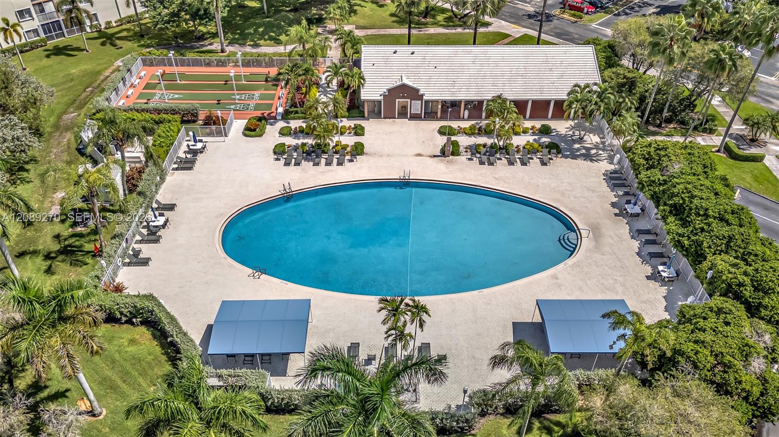 Community pool surrounded by lounge chairs, palm trees, a clubhouse, and a fenced sports court.