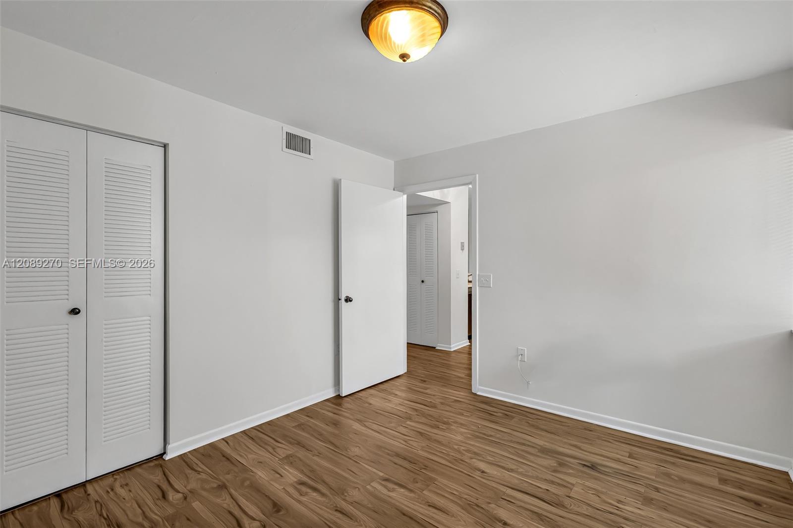 Empty bedroom with wood-look flooring, louvered closet doors, and an open doorway.