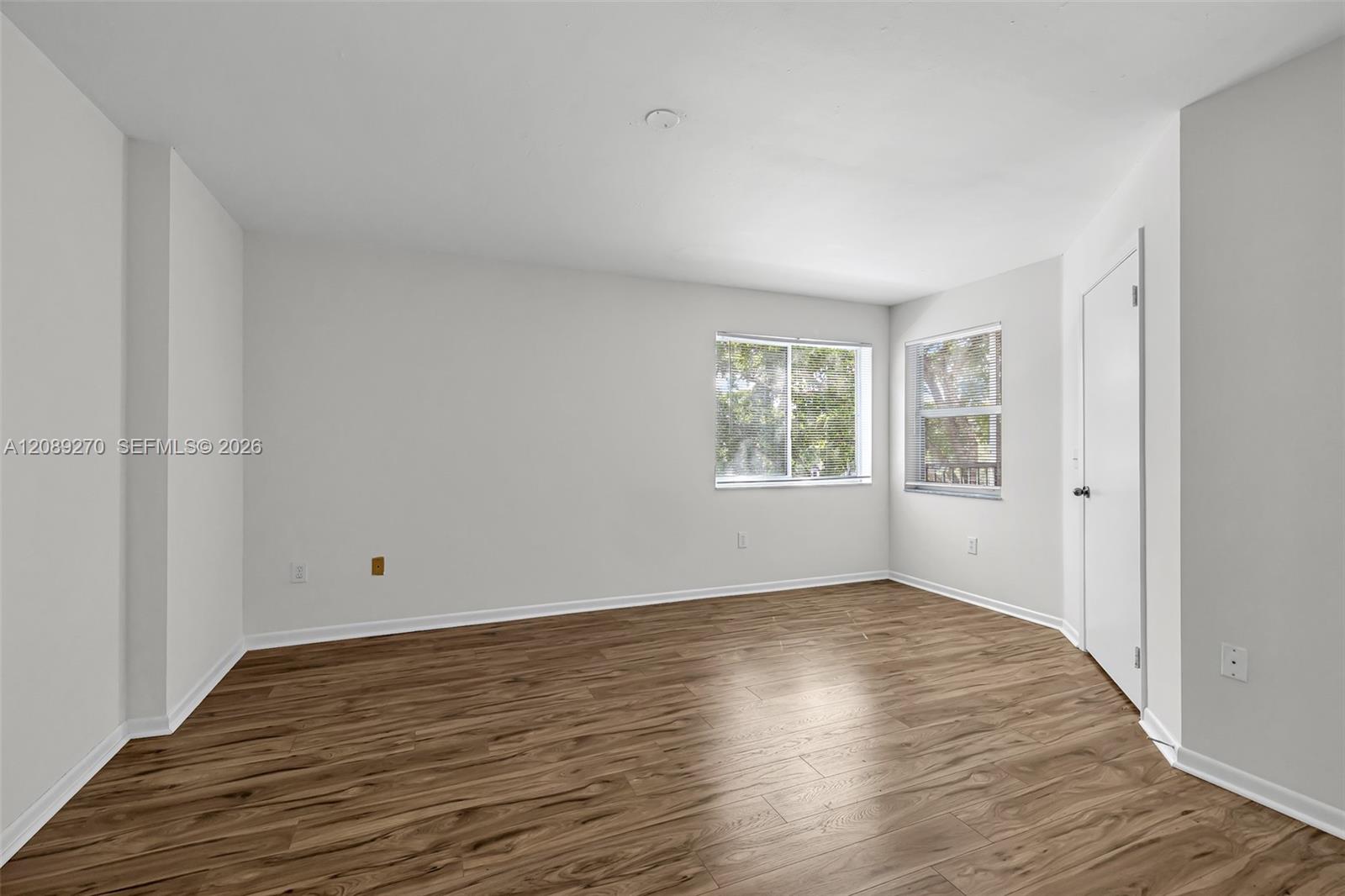 Vacant room with wood-look floors and two windows.