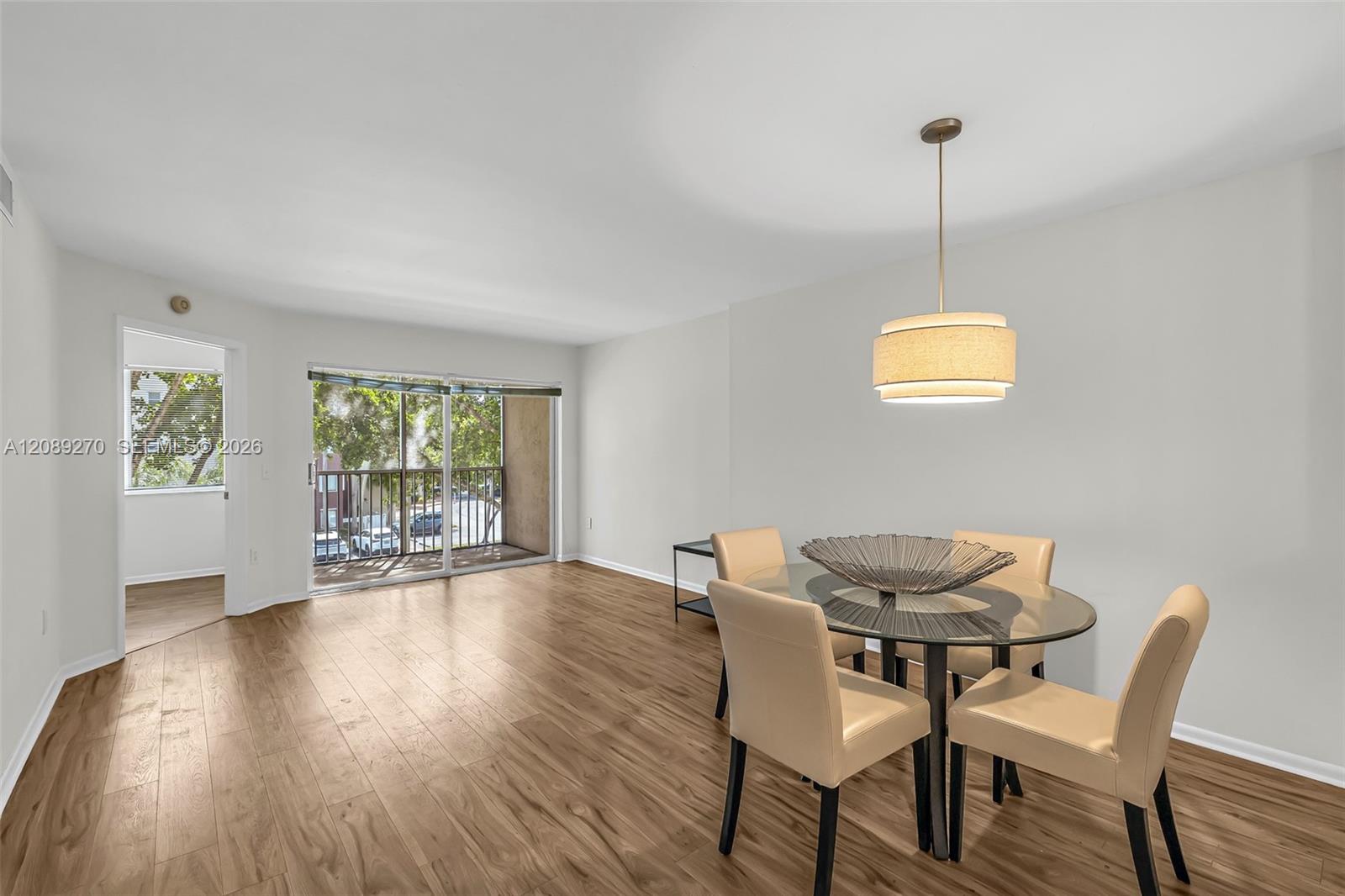 Condo dining area with a glass table, beige chairs, wood-look flooring, and sliding doors to a balcony.