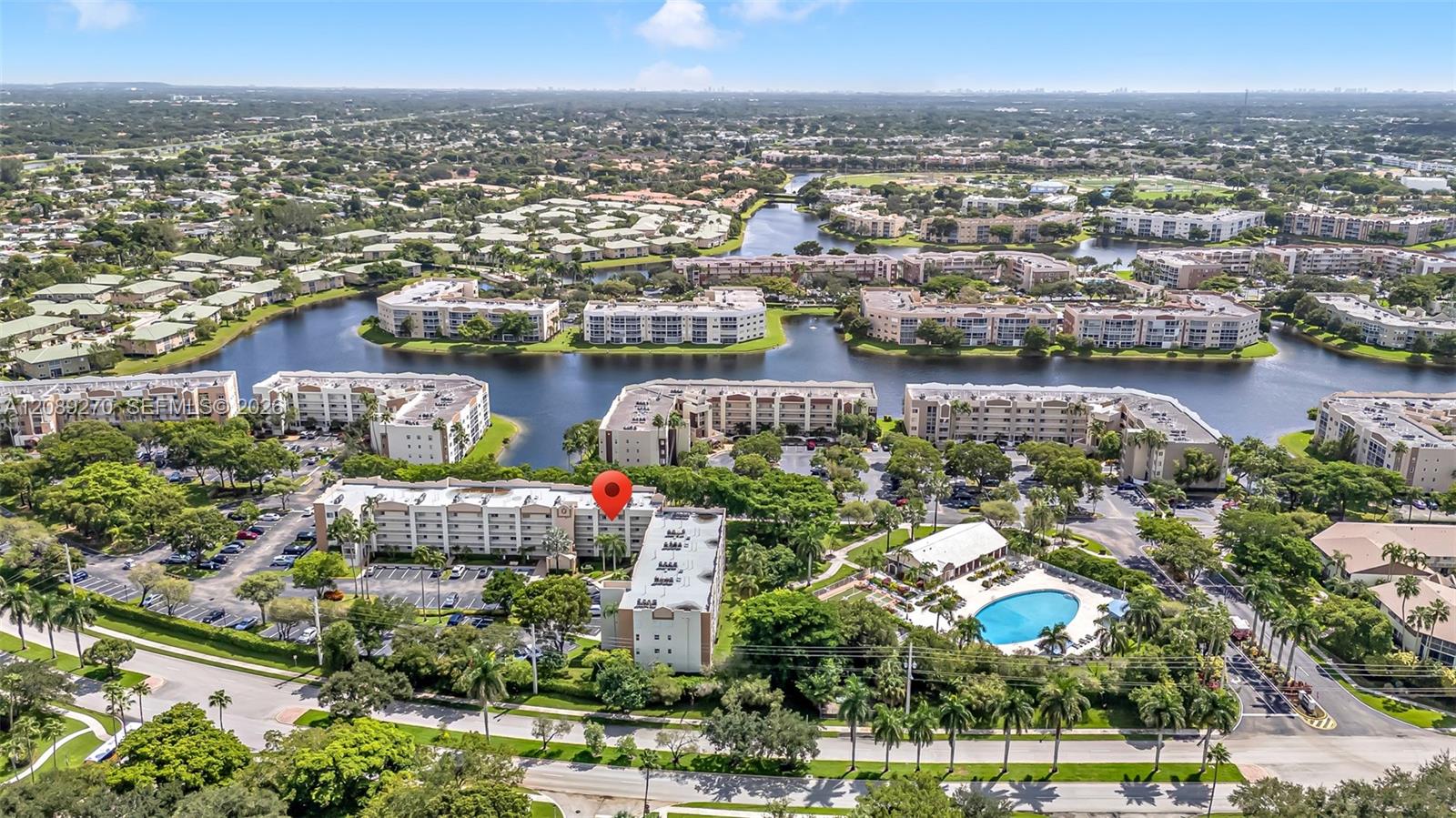 Aerial view of a marked condominium building beside winding waterways, with a pool and other buildings nearby.