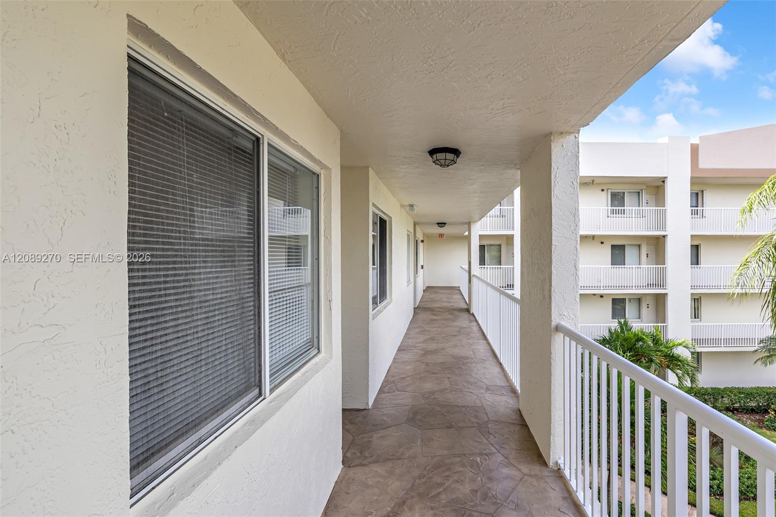 Covered condo walkway with a tiled floor, white railing, and windows overlooking the courtyard.