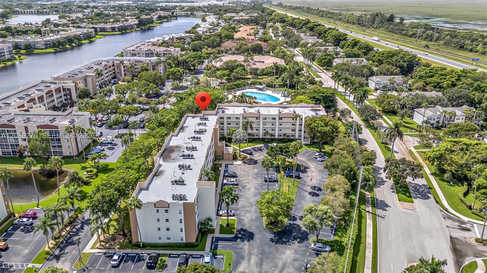 Aerial view of a condominium complex with a pool, parking areas, and surrounding waterways.