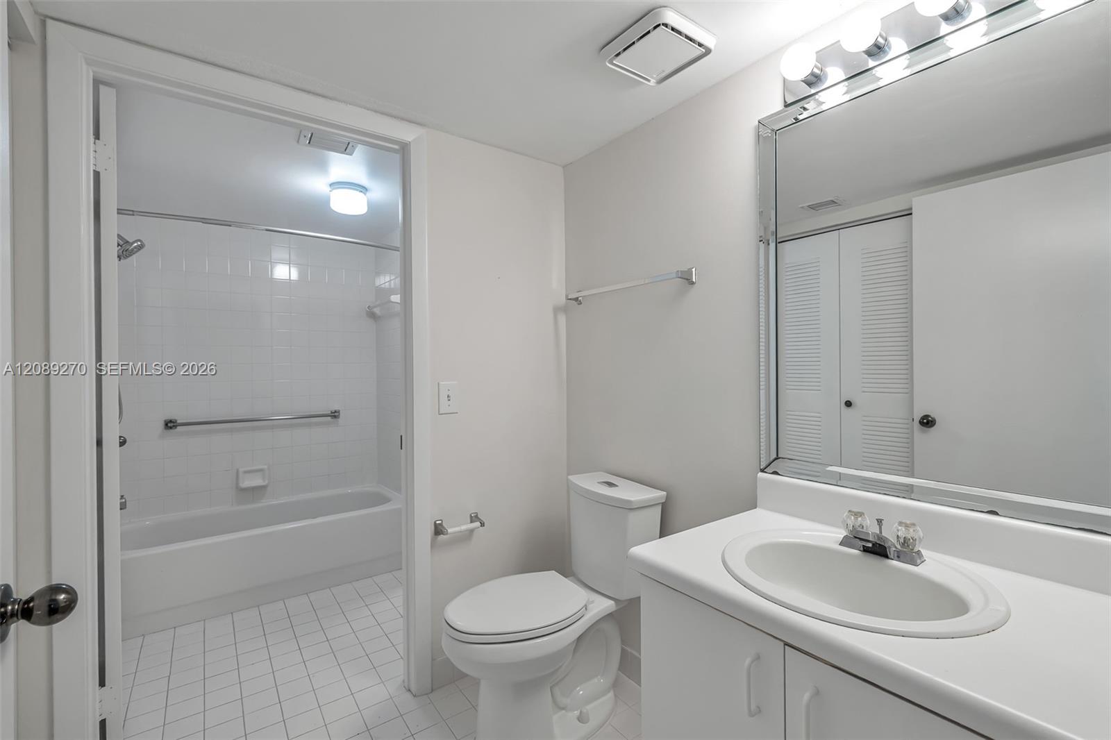 Bathroom with a tiled tub-shower alcove, white toilet, and sink vanity beneath a large mirror.
