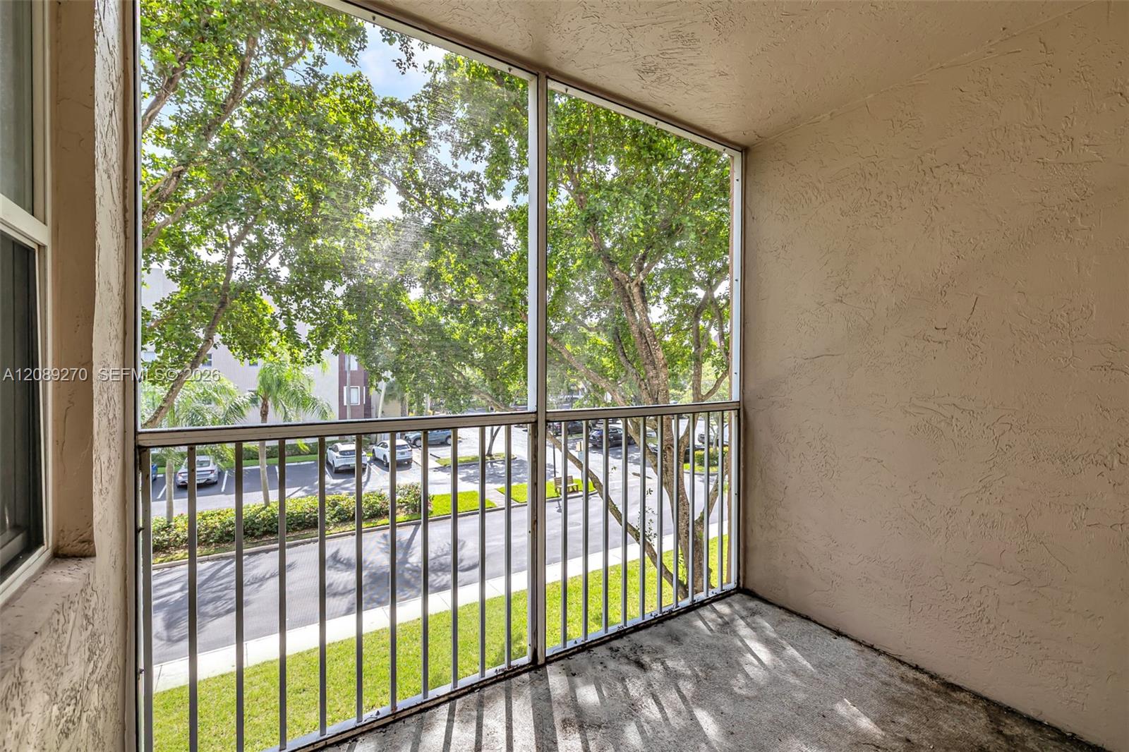Empty enclosed balcony overlooking leafy trees and a parking area.