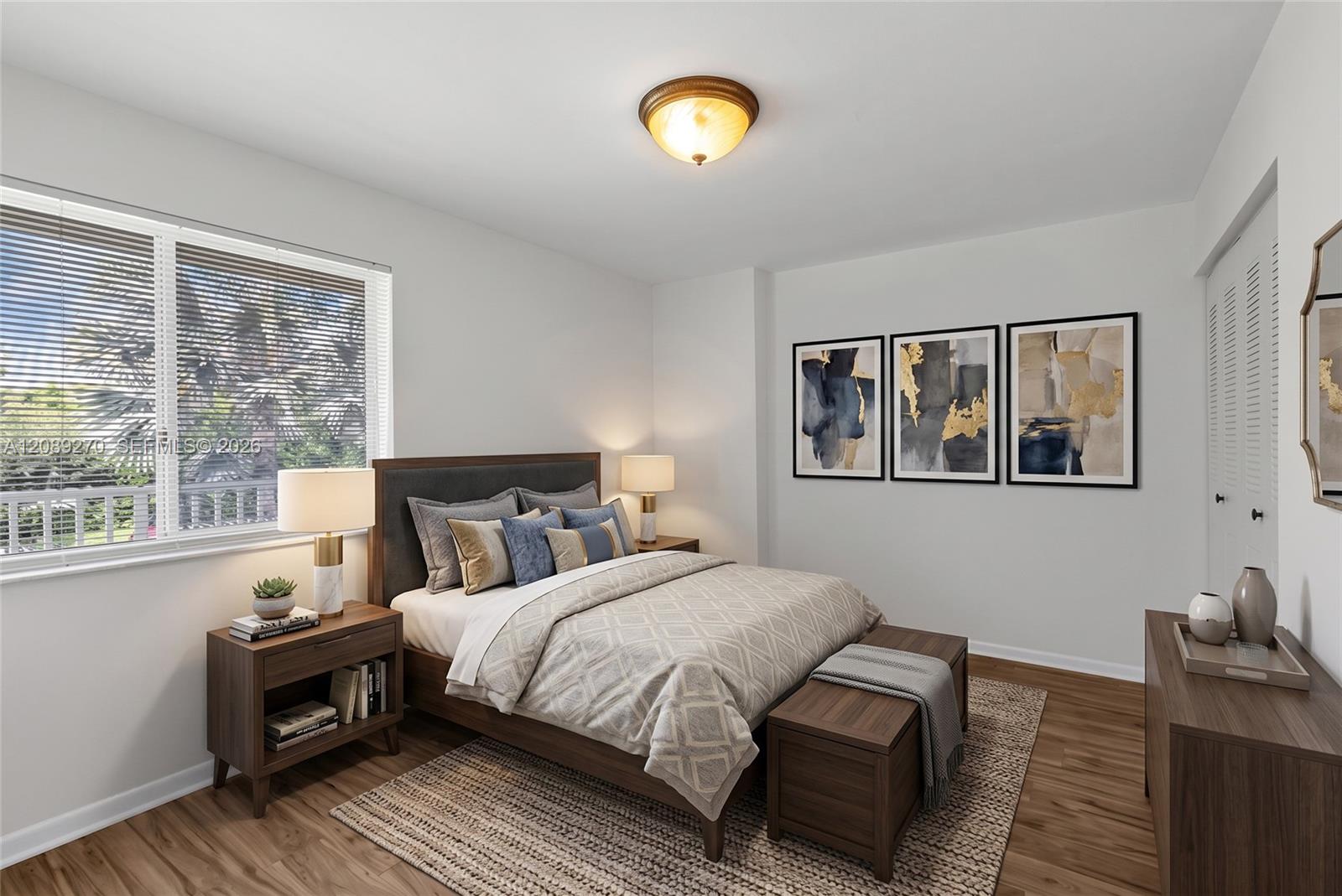 Furnished bedroom with neutral bedding, dark wood furniture, and a large window with blinds.