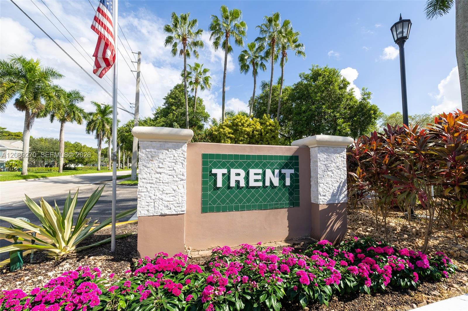 Trent community entrance sign framed by palm trees and bright pink flowers.