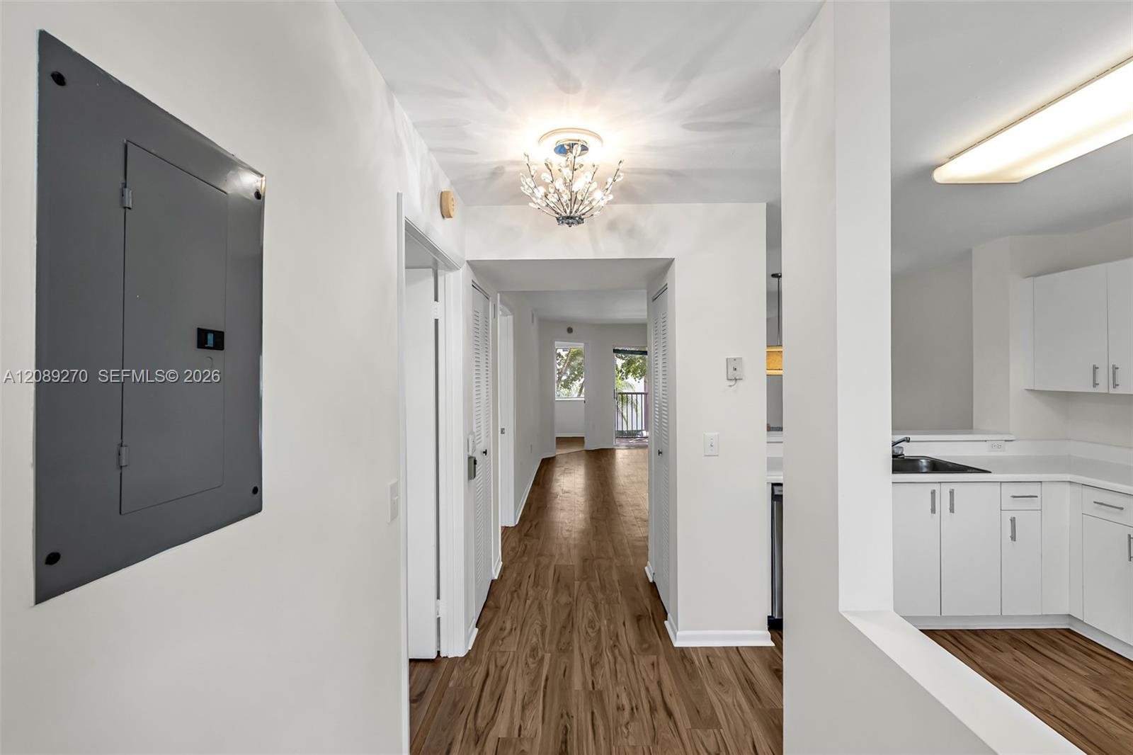 Apartment hallway with wood-look flooring, a chandelier, and part of a white kitchen.