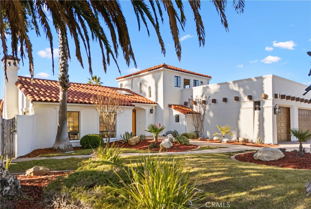 White stucco home with red tile roofs, palm trees, and landscaped front yard.