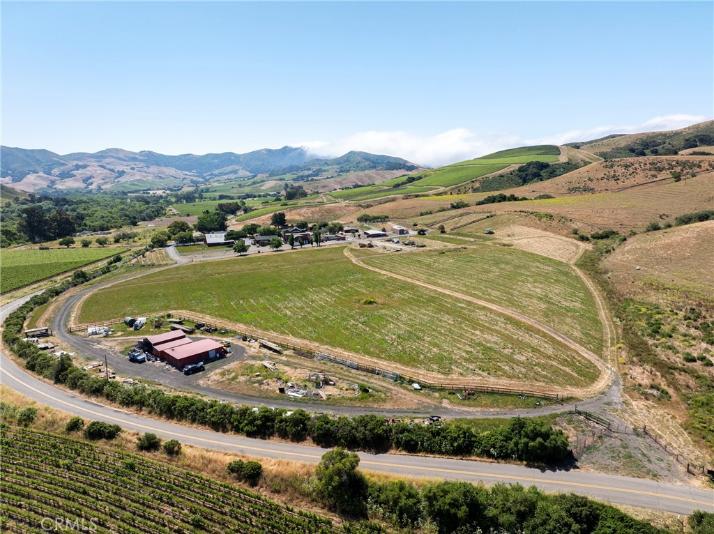 Rural property with cultivated fields, vineyard rows, outbuildings, and distant mountains.