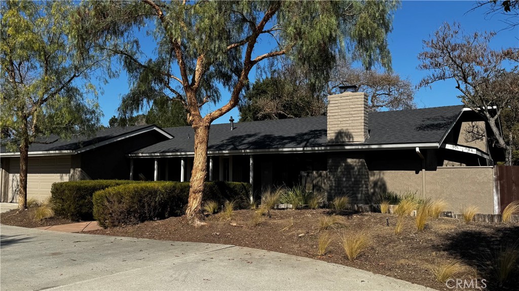 Single-story home with a dark roof, brick chimney, attached garage, and landscaped front yard.