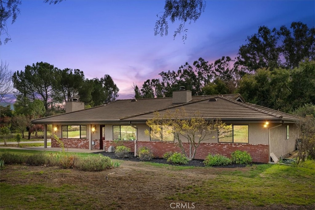 Single-story home with a tiled roof and brick-and-stucco exterior, photographed from the yard at dusk.