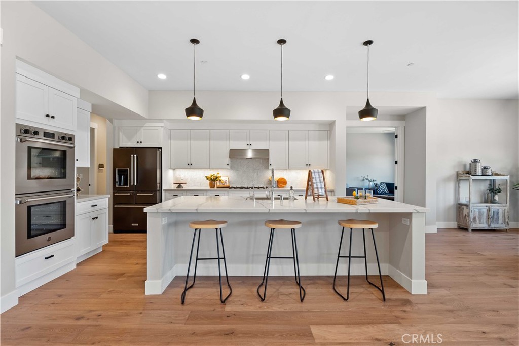 Open kitchen with a large island, three stools, white cabinets, and stainless steel appliances.