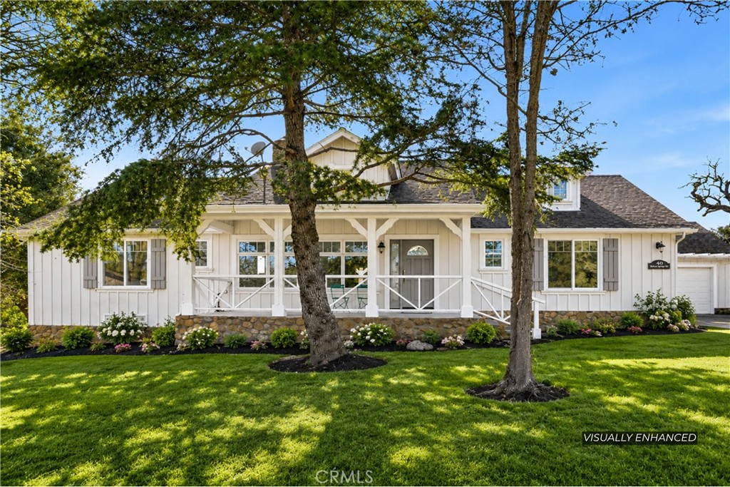 White single-story house with a covered porch, stone foundation, and two mature trees across the lawn.