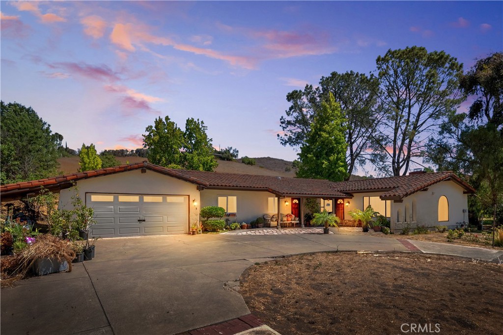 Single-story stucco home with a tiled roof and broad driveway, photographed at dusk.