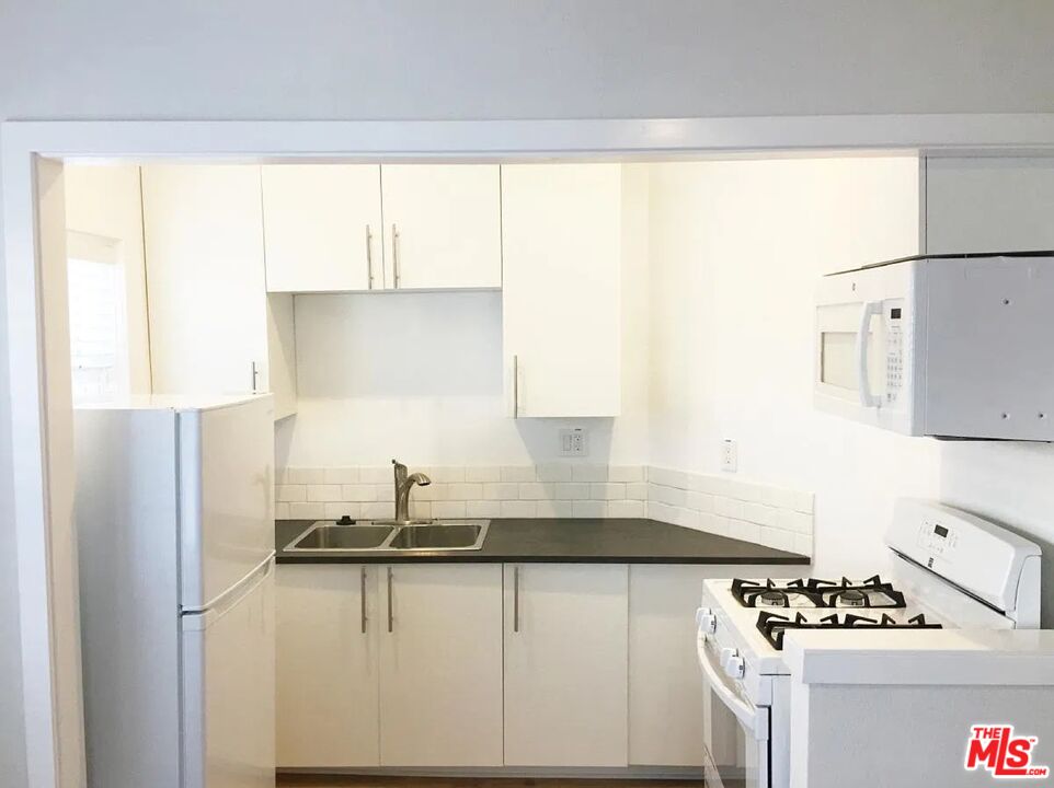 Compact kitchen with white cabinets, dark counters, and stainless steel appliances.