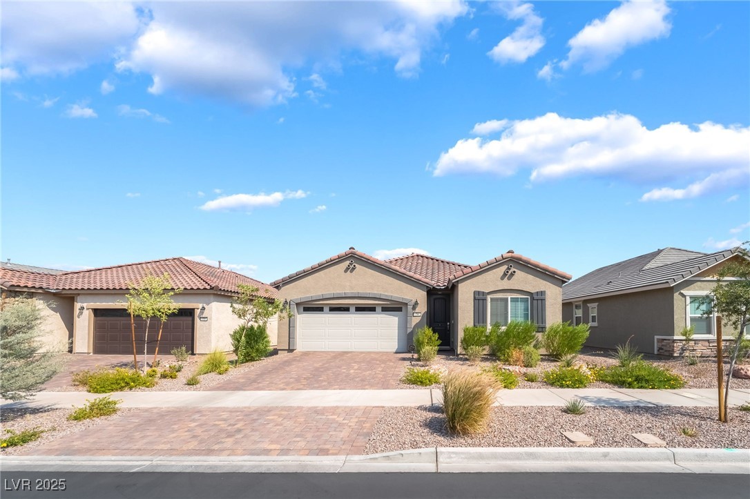 Single-story stucco home with a two-car garage, paver driveway, and desert landscaping.