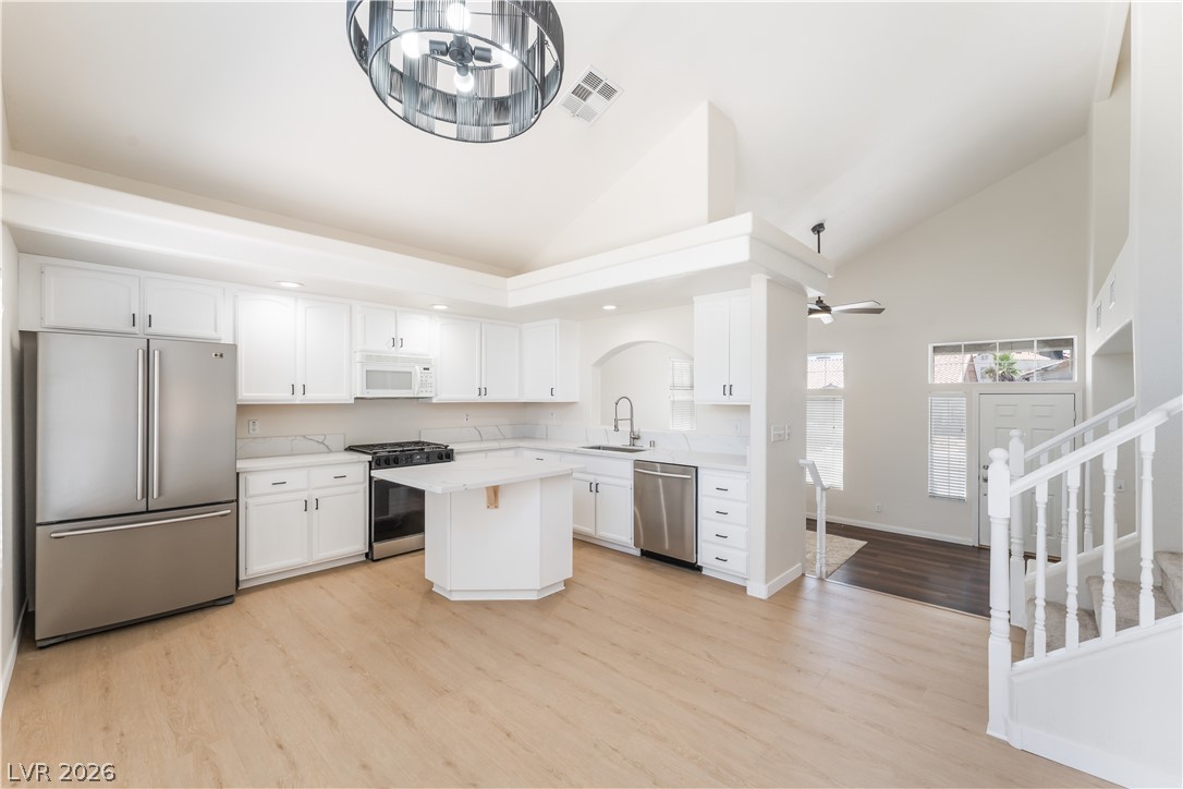 Open-plan kitchen with white cabinetry, stainless appliances, and a central island beneath a high ceiling.