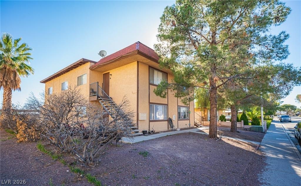 Two-story tan stucco home with a red tiled roof, exterior staircase, and mature trees.