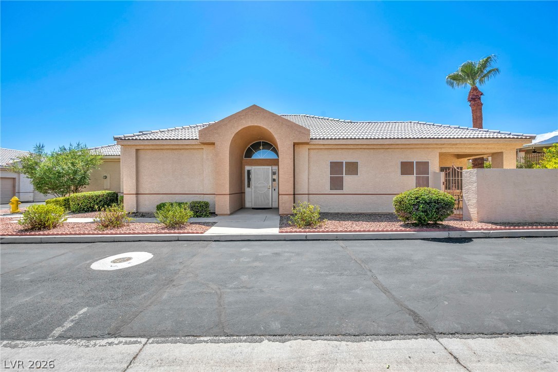 Single-story stucco home with an arched entry, tile roof, desert landscaping, and palm tree.