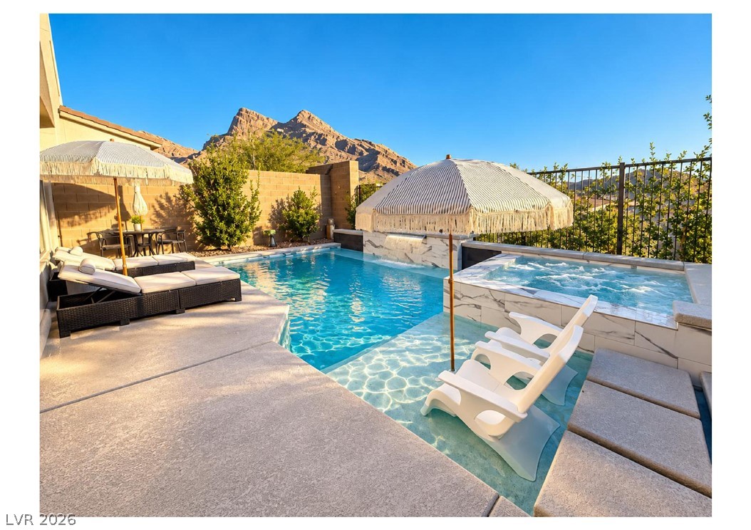 Backyard pool and raised spa with in-water loungers and mountains in the background.
