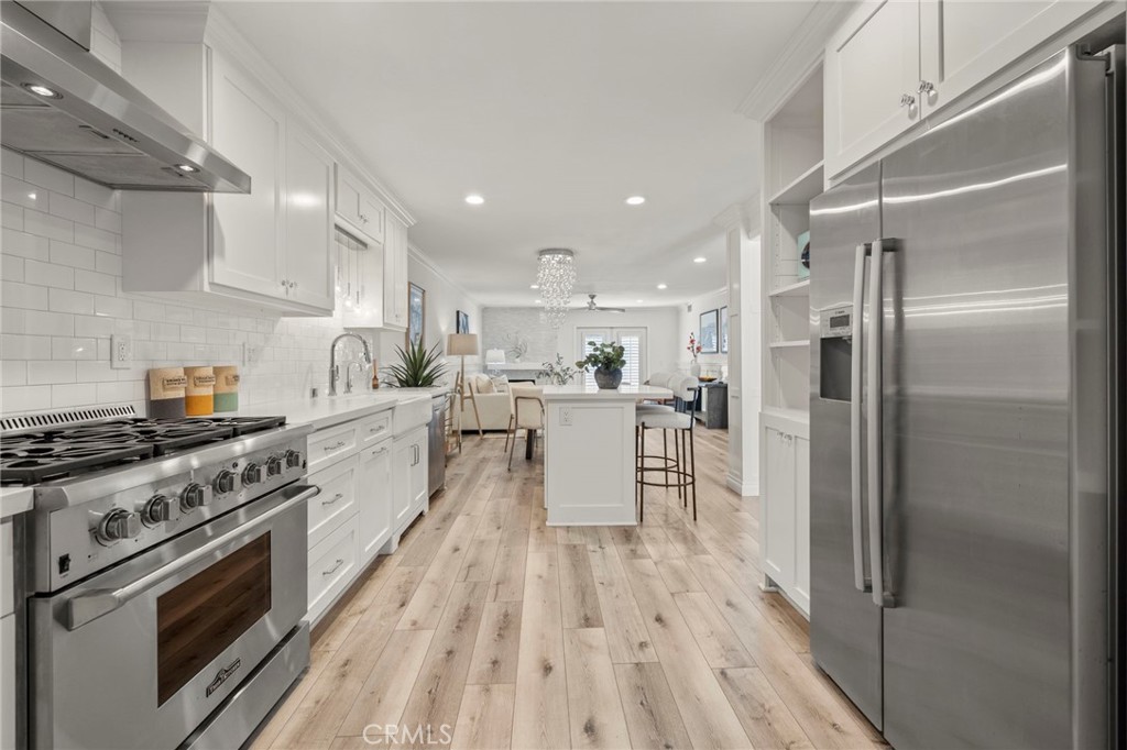 Staged kitchen with white cabinetry, stainless steel appliances, and a central island opening to the living area.