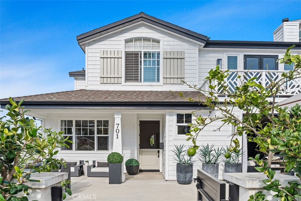 White two-story house with gray shutters, an upper balcony, and a furnished front patio.