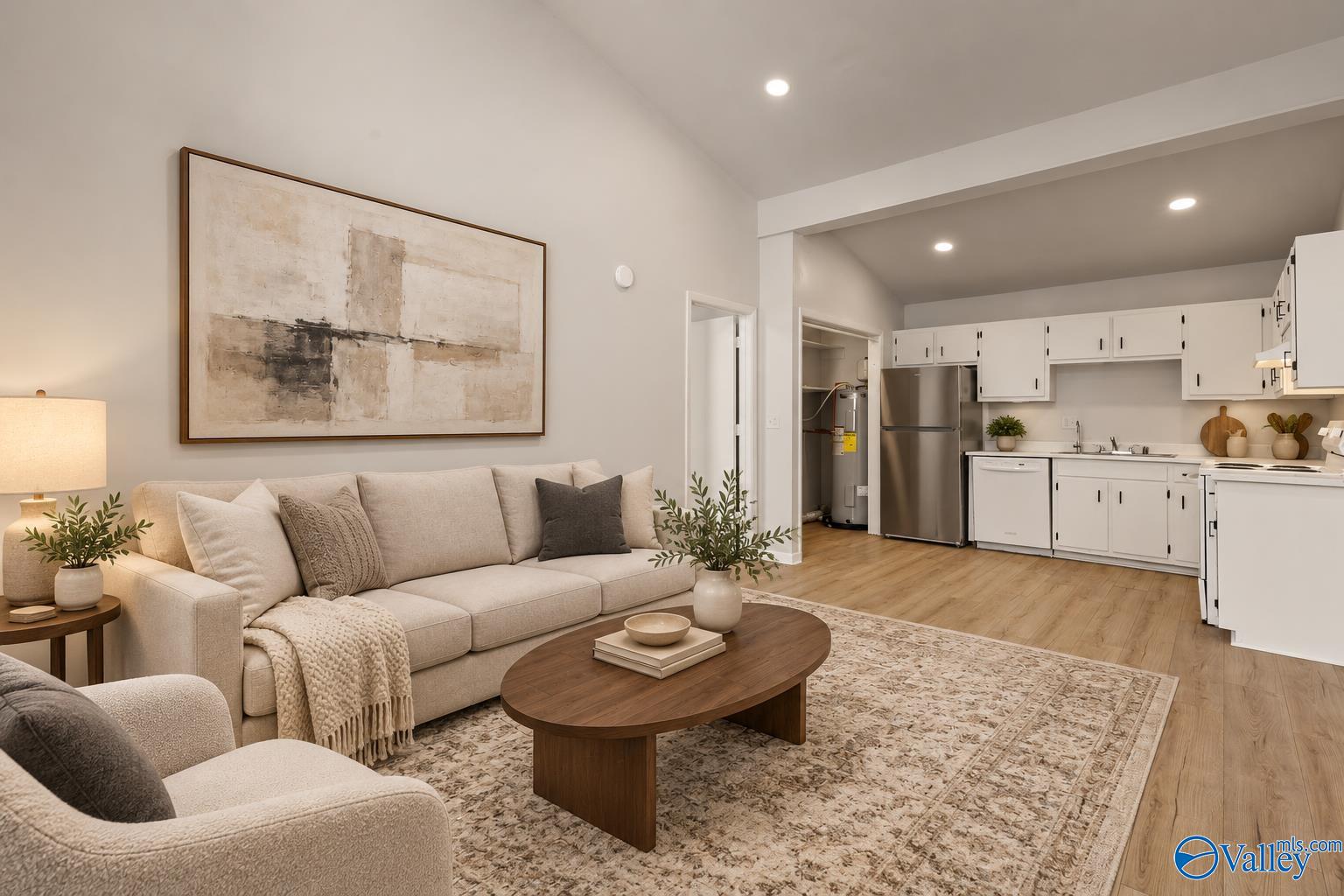 Furnished living room opens to a white-cabinet kitchen, with cream sofa and wooden coffee table.