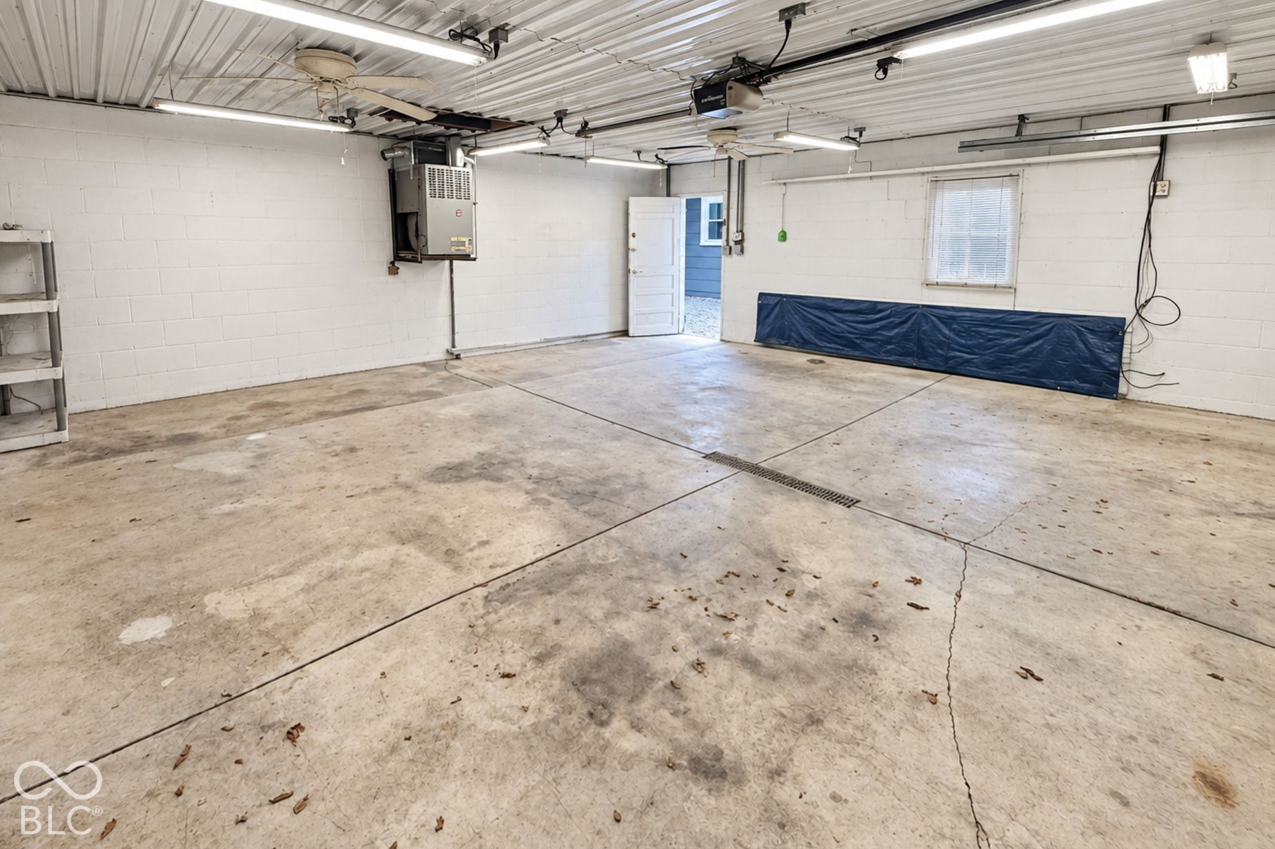 Empty garage with a stained concrete floor, overhead door tracks, and an open side door.