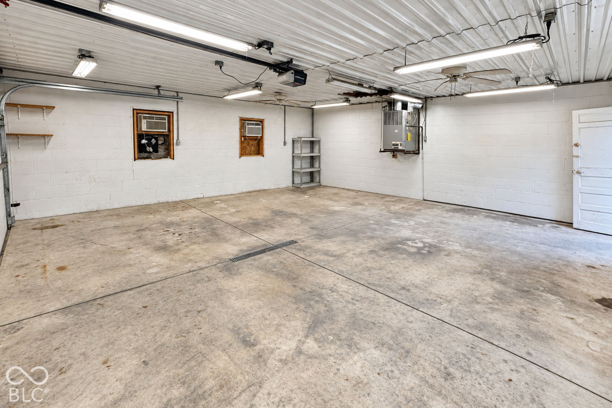 Empty garage with a stained concrete floor, fluorescent lights, and a wall-mounted furnace.