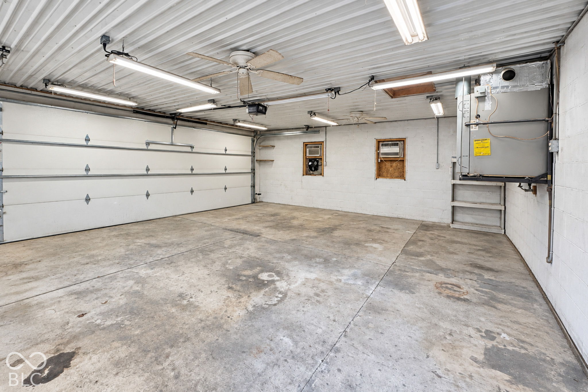 Vacant garage with a wide overhead door, concrete floor, and fluorescent ceiling lights.