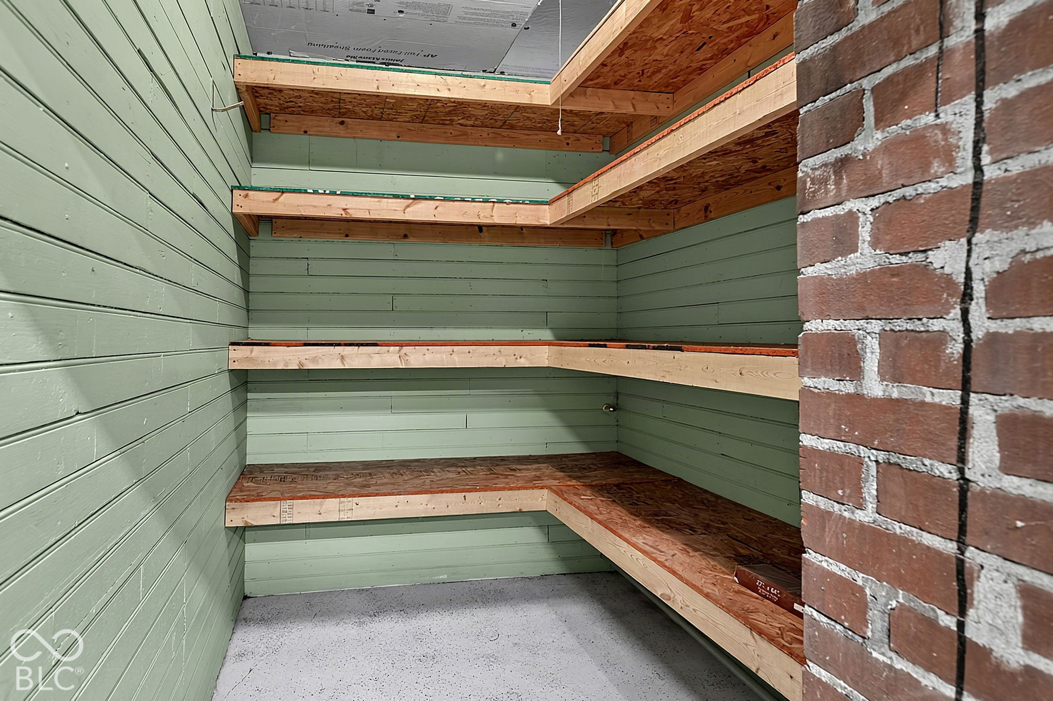 Storage room with green walls, unfinished wooden shelves, and a concrete floor.