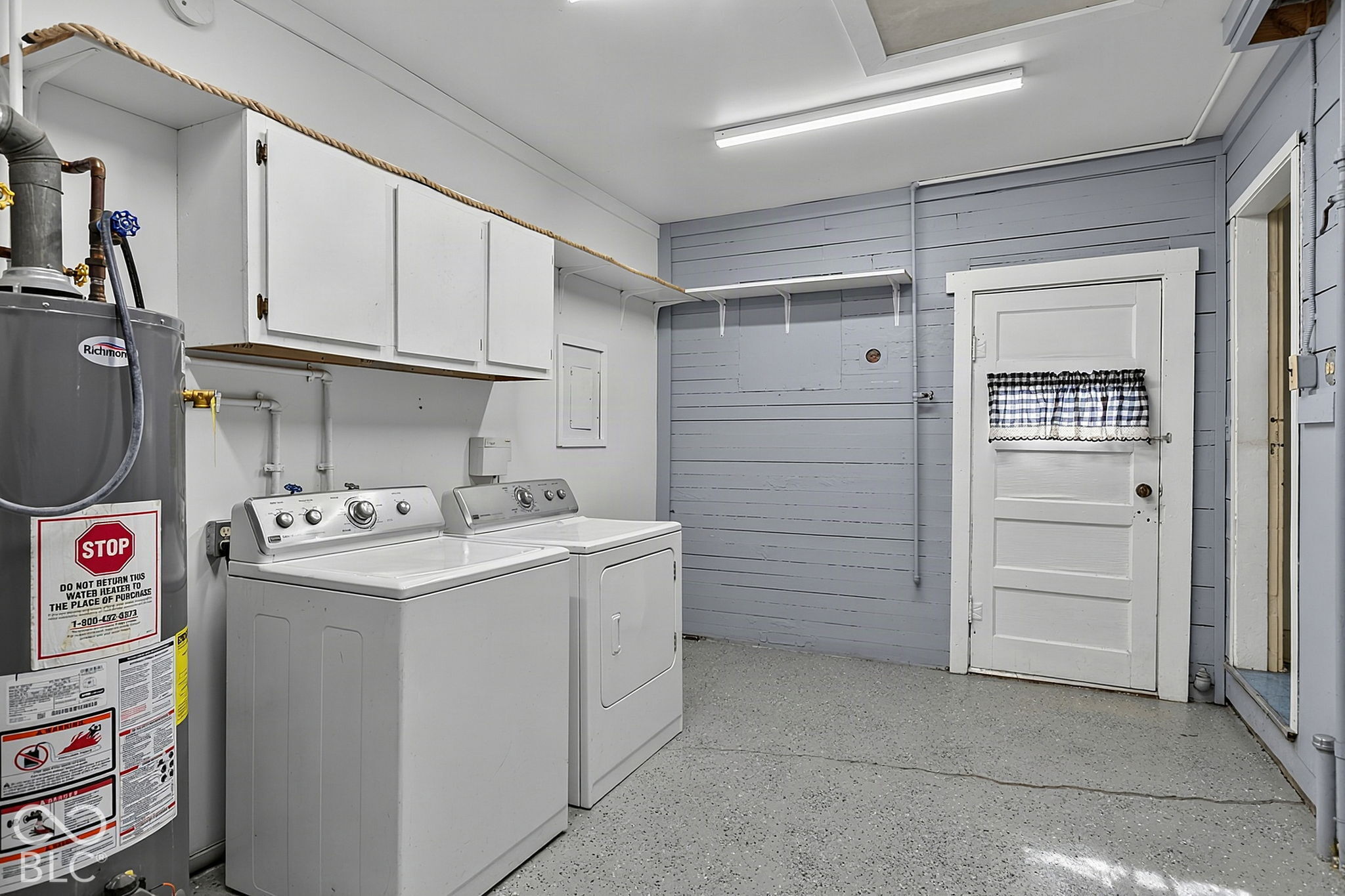 Laundry room with washer, dryer, and water heater beneath white storage cabinets.