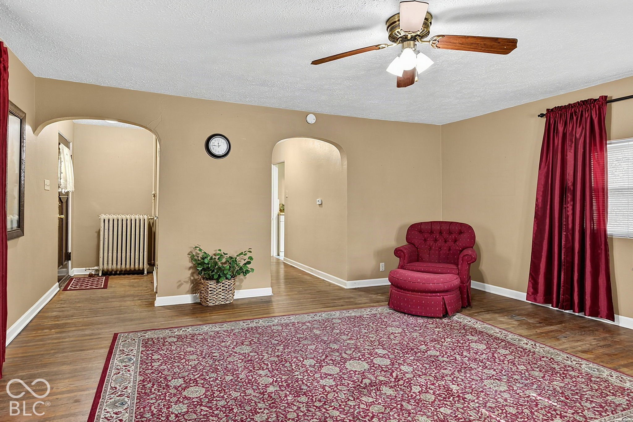 Living room with hardwood floors, arched openings, and a red armchair beside a large patterned rug.