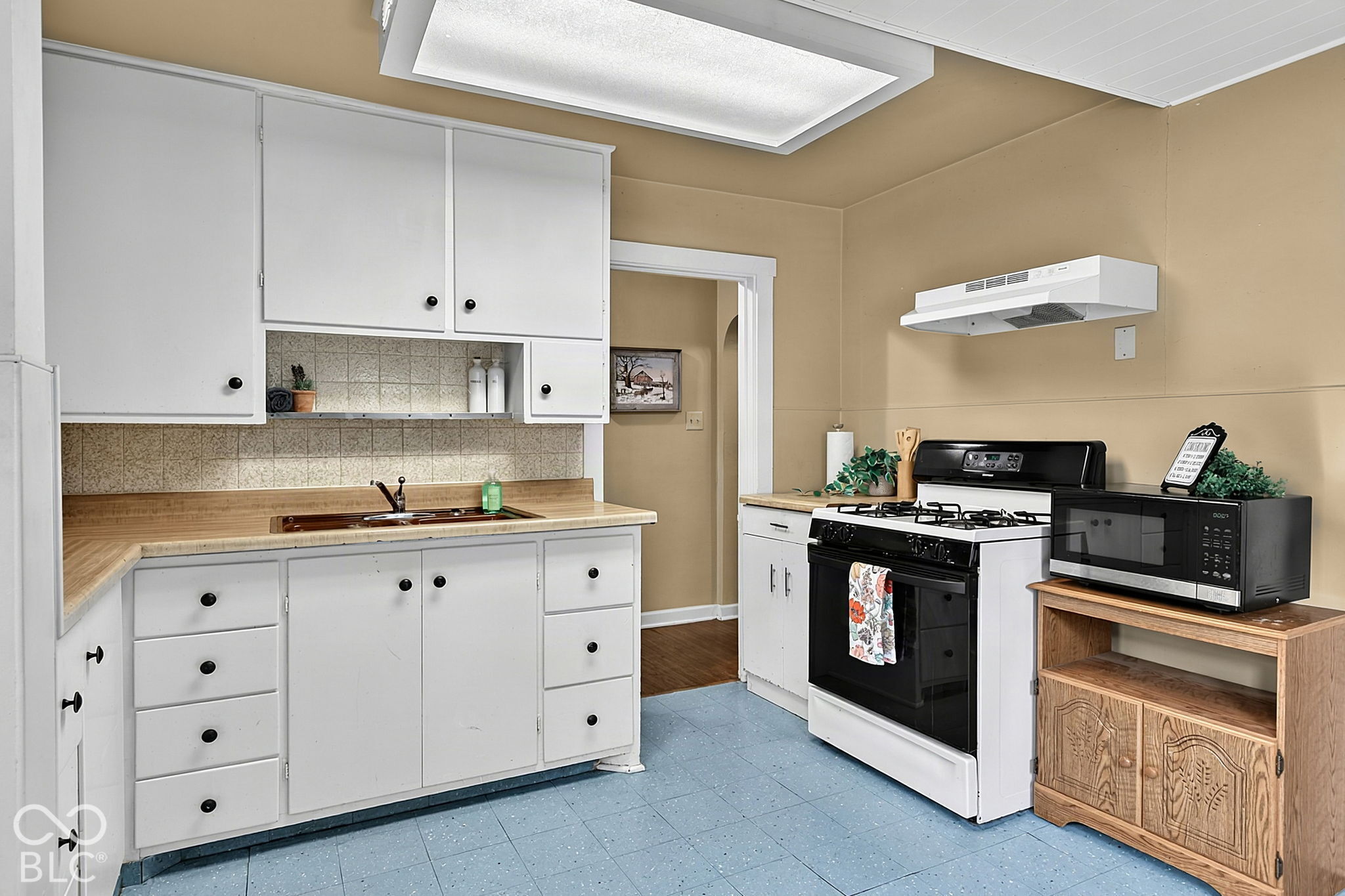 Kitchen with white cabinets, tan counters, blue tile floor, and a black-and-white gas range.