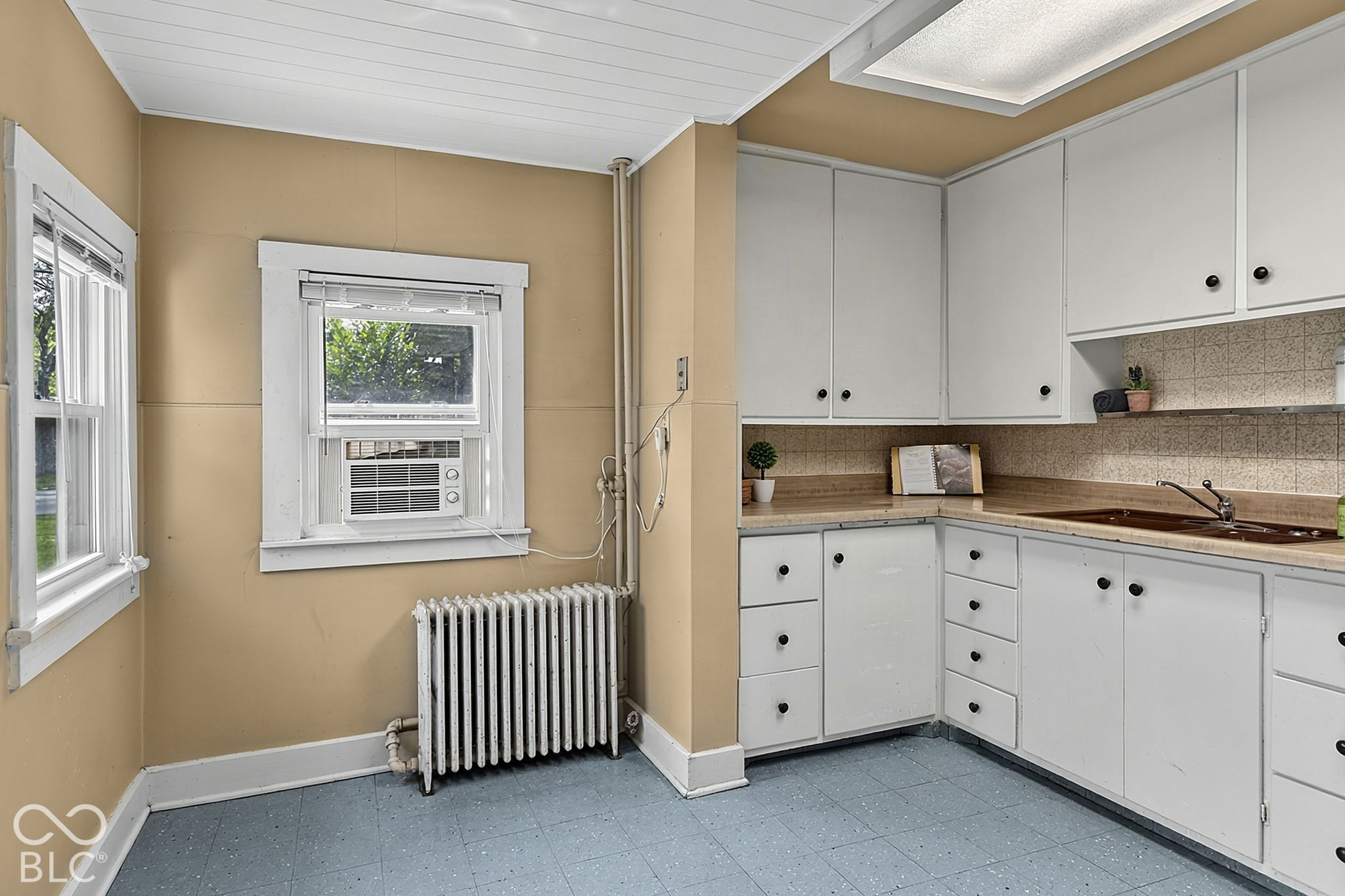 Kitchen with white cabinets and a brown countertop, plus a window air conditioner above a radiator.