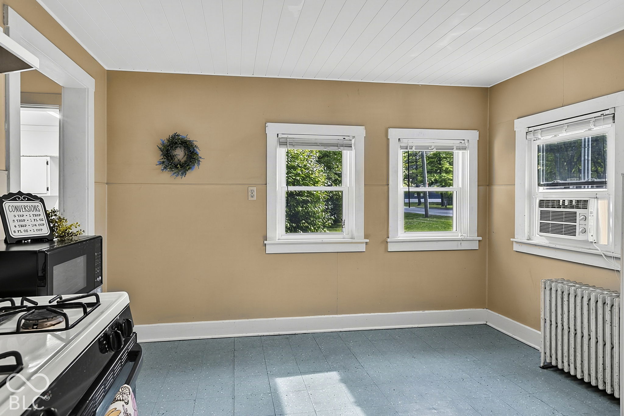 Kitchen with tan walls, blue tile flooring, three windows, and a gas stove.