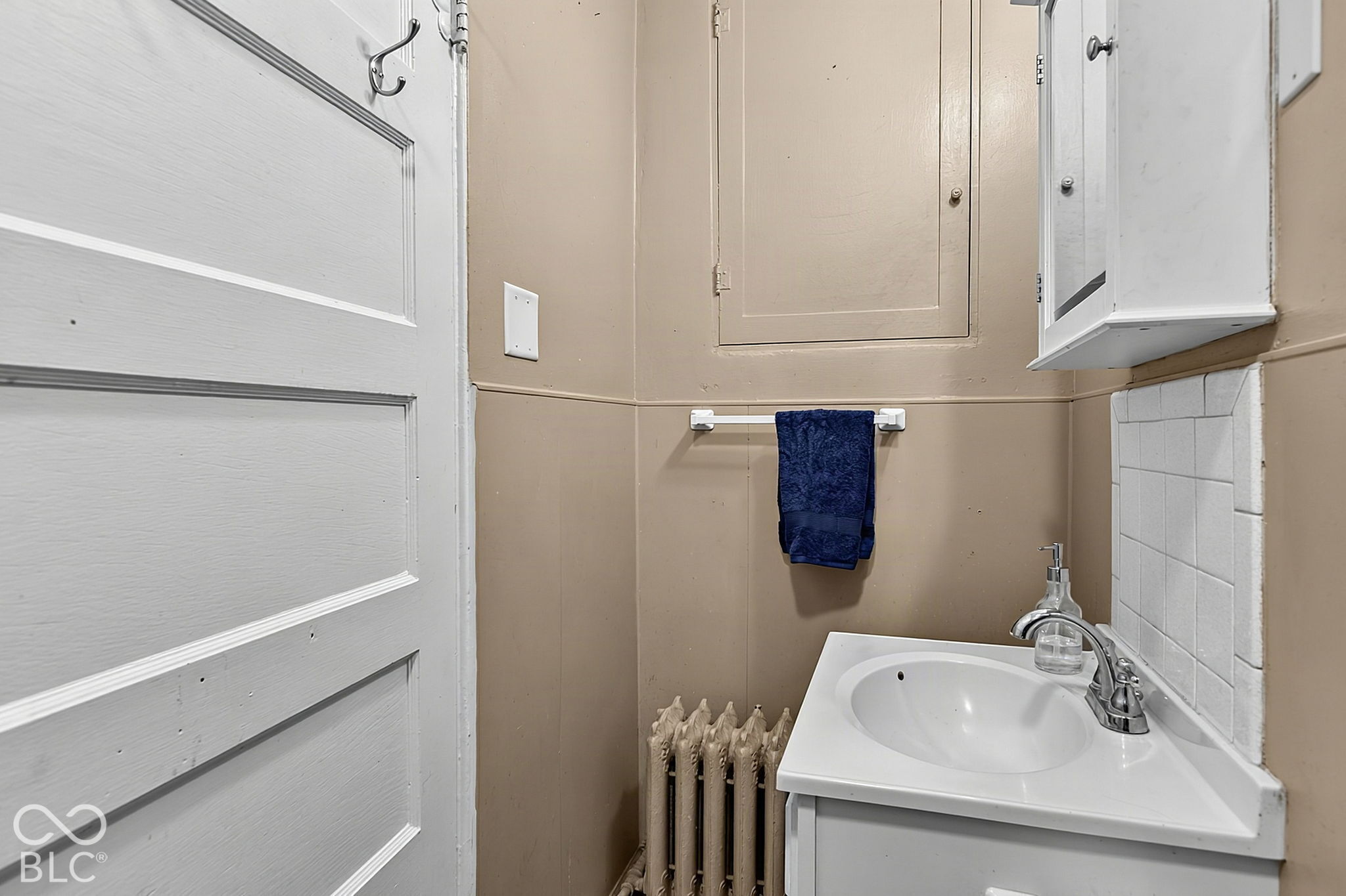 Small bathroom with a white sink, wall-mounted medicine cabinet, navy towel, and exposed radiator.