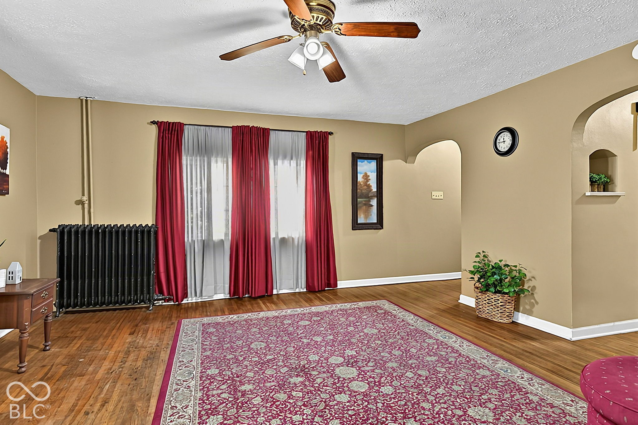 Living room with hardwood floors, a large patterned rug, red curtains, and a black radiator.