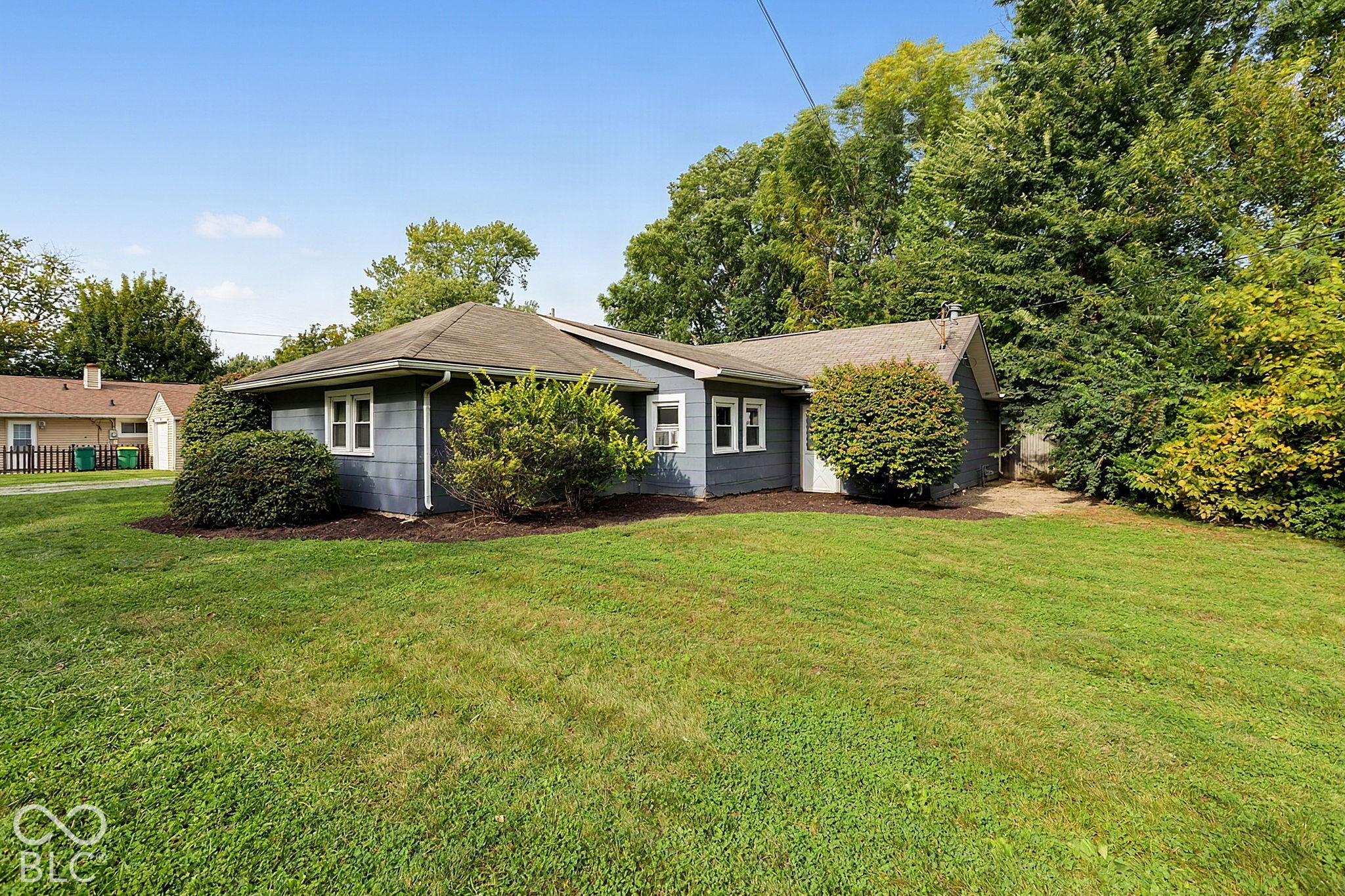 Gray single-story home with white-trimmed windows, landscaped shrubs, and a broad green lawn.