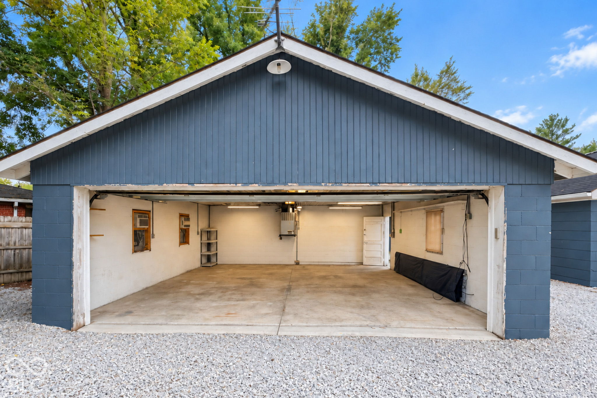 Open garage with blue siding, a wide concrete floor, and a gravel apron.