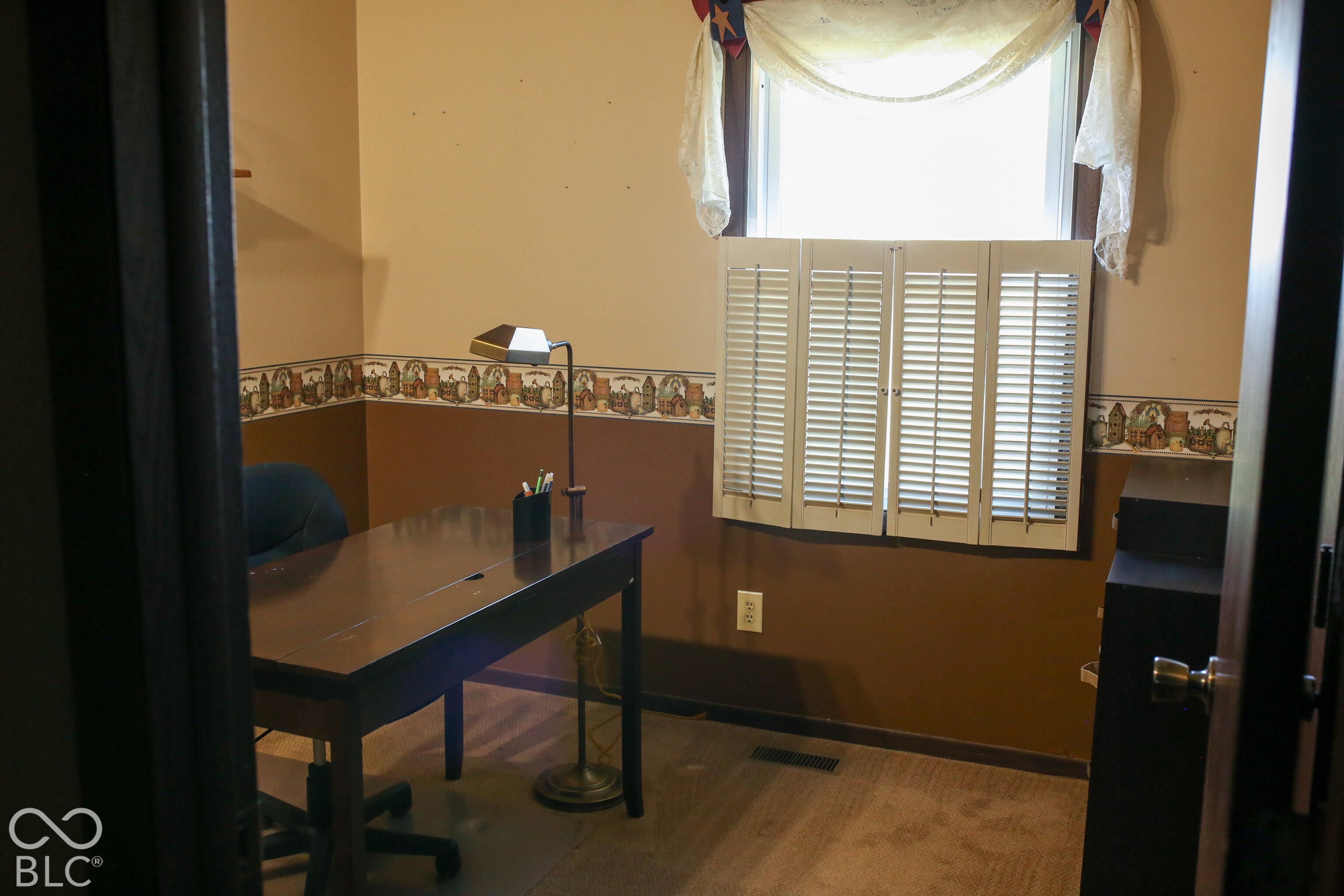 Home office with a dark desk, brown walls, decorative border, and window shutters.
