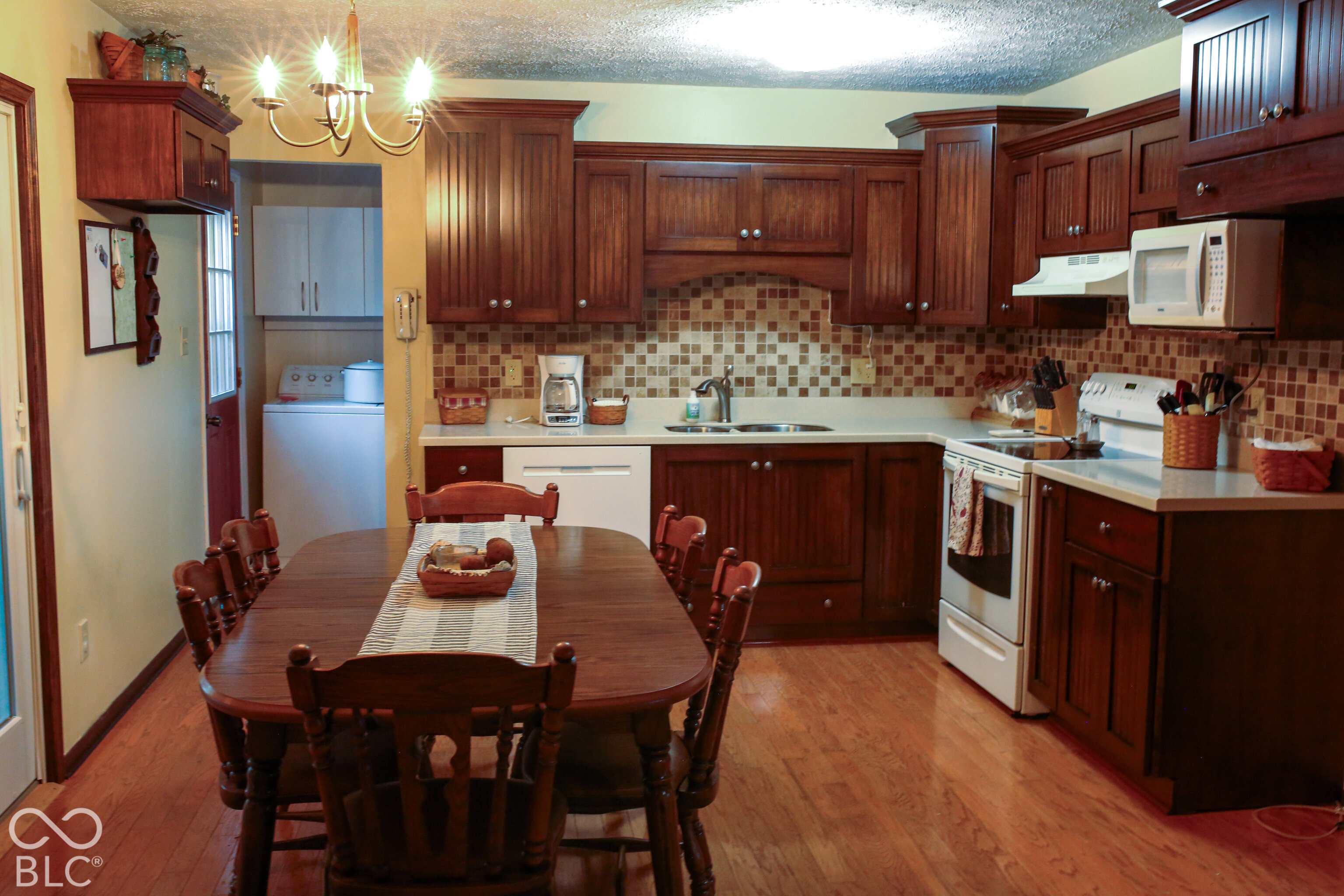 Kitchen with dark wood cabinets, tiled backsplash, white appliances, and a wooden dining table.
