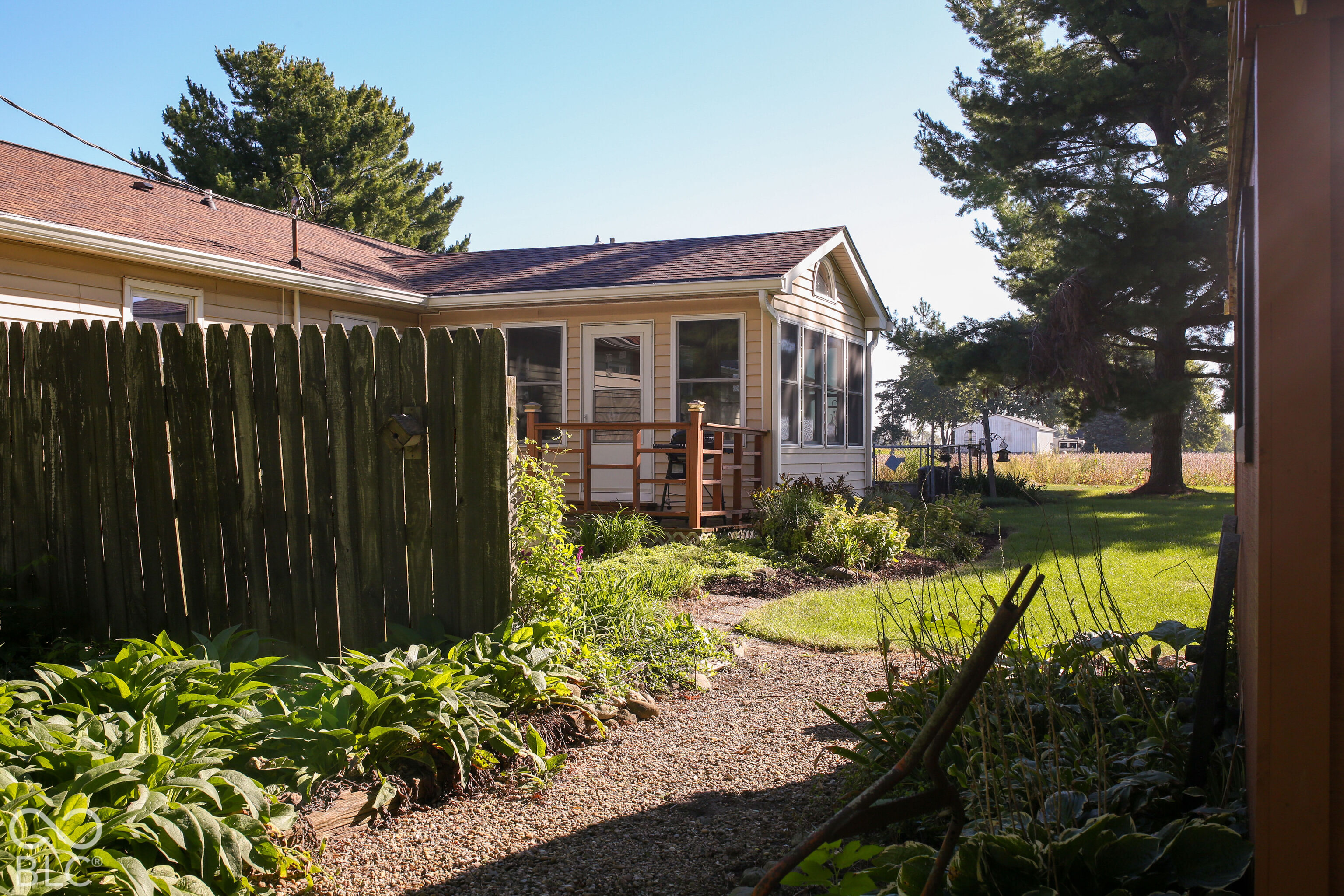Home exterior with a small deck, landscaped garden, gravel path, and tall wooden fence.