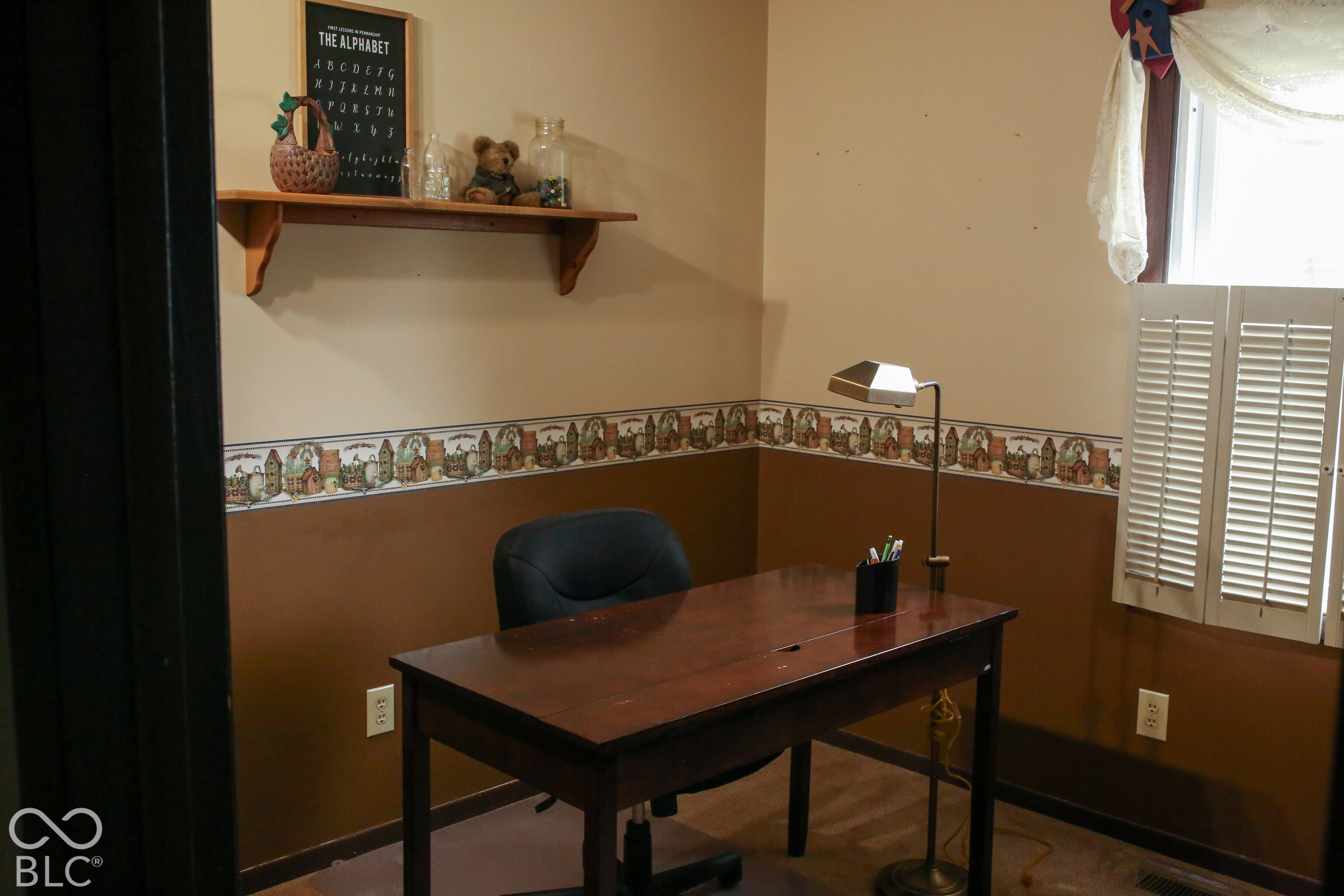 Home office with a dark wooden desk, floor lamp, and window with white shutters.