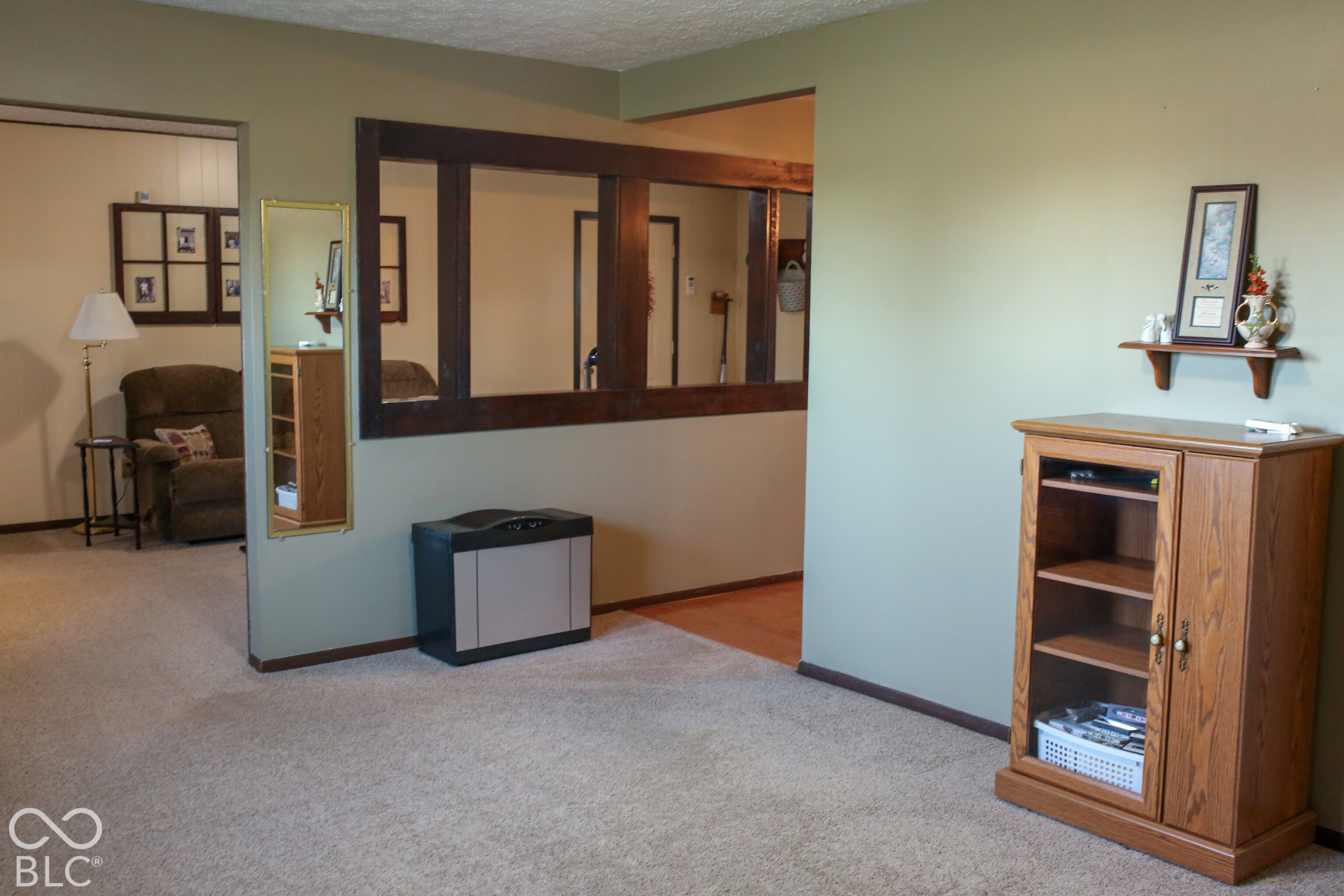 Living room with beige carpeting, a dark wood pass-through, and a wooden display cabinet.