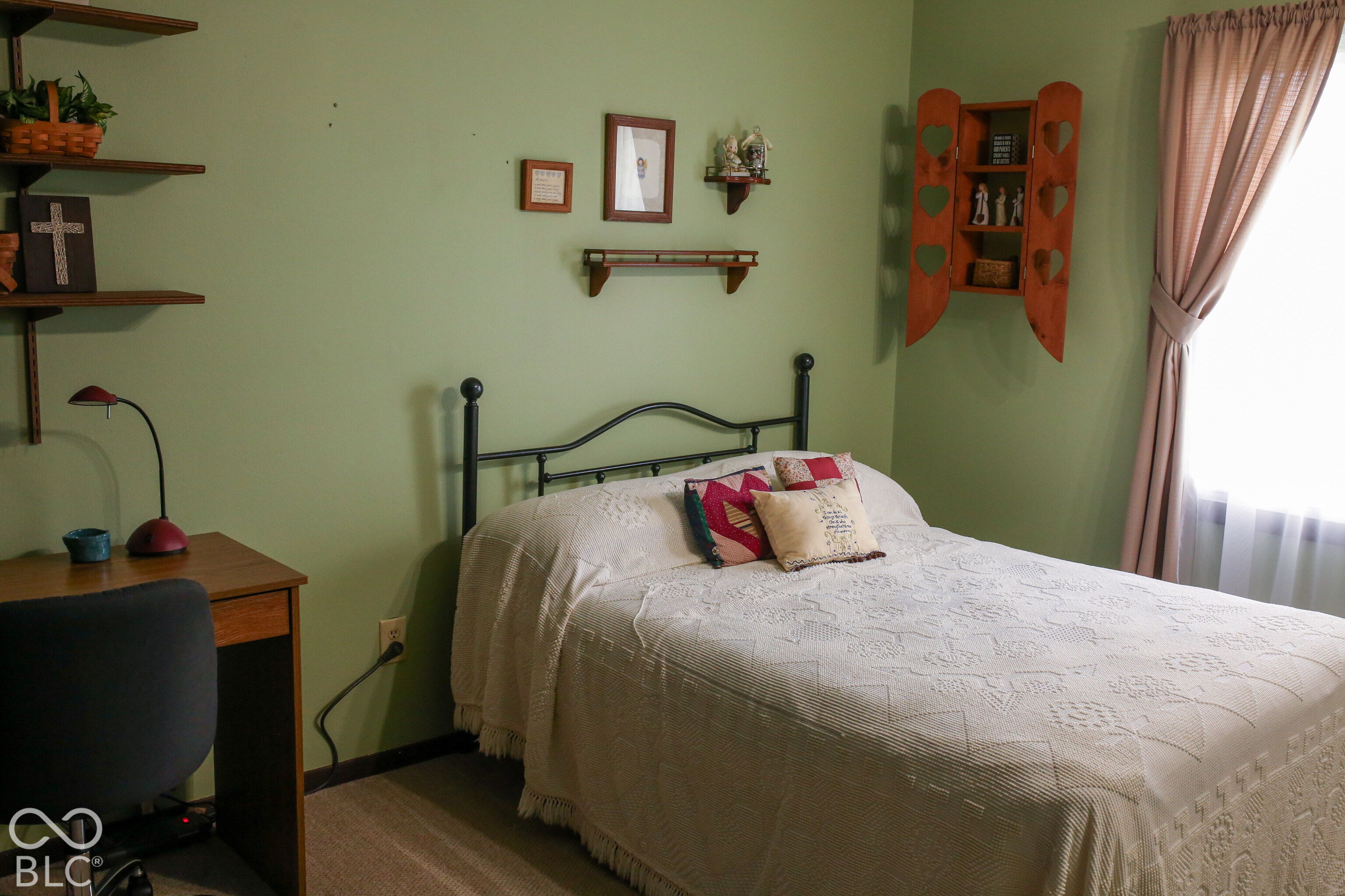 Bedroom with a white quilted bed, black metal headboard, green walls, and a bright curtained window.