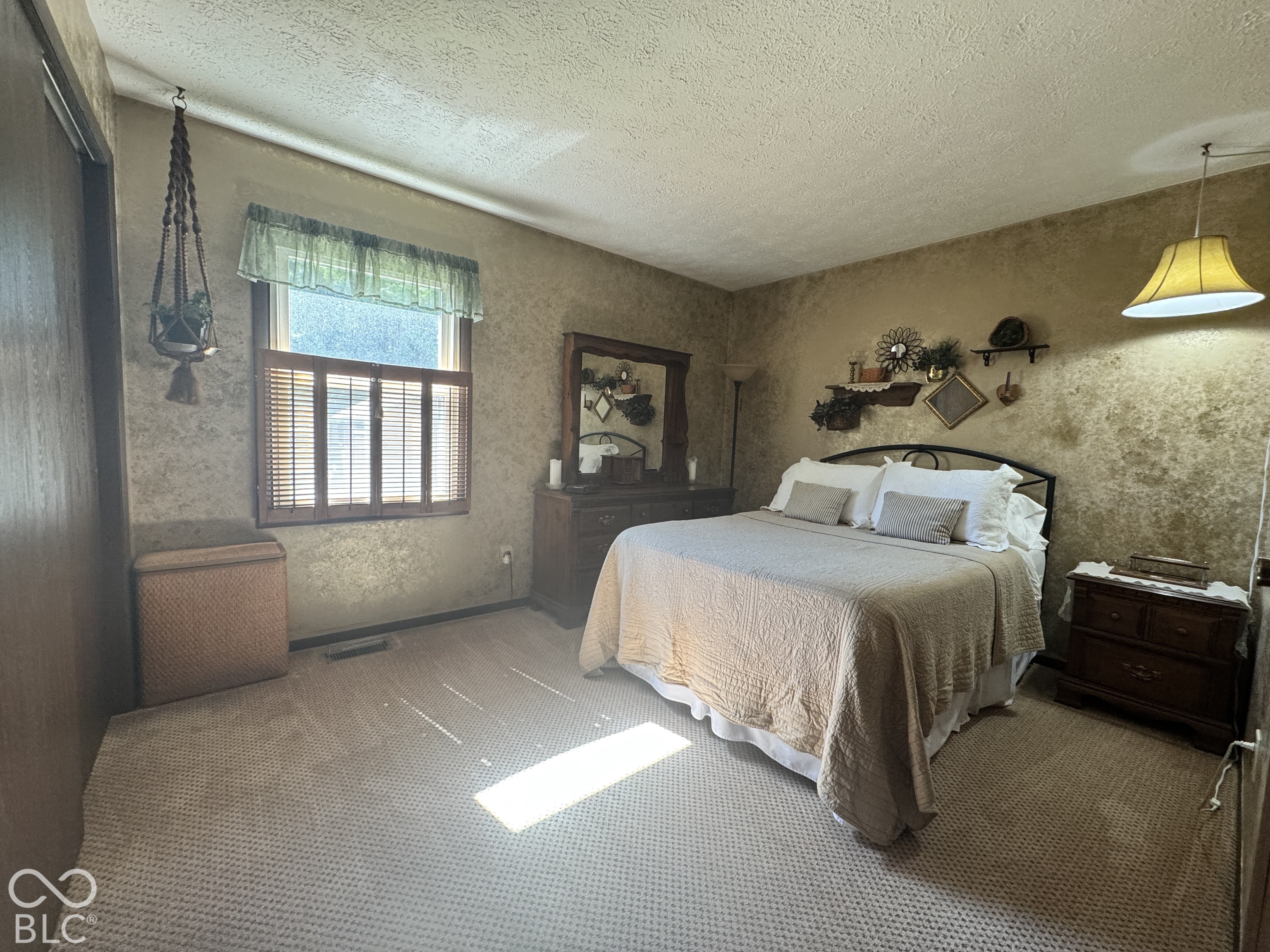 Bedroom with a double bed, wooden furnishings, carpet, and sunlight streaming through a window.