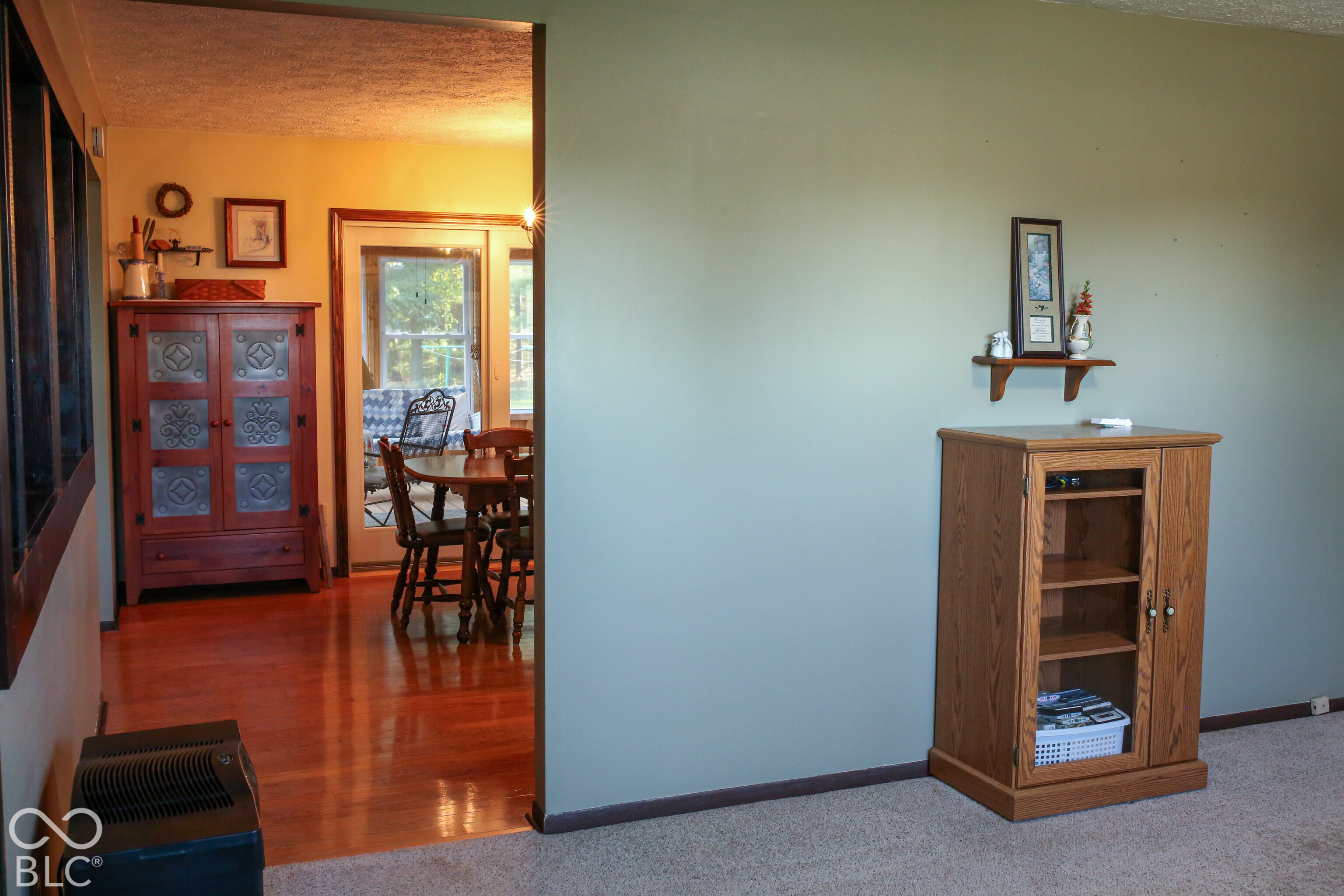 Furnished living area with wooden media cabinet, opening to a dining area with hardwood floors and a window.